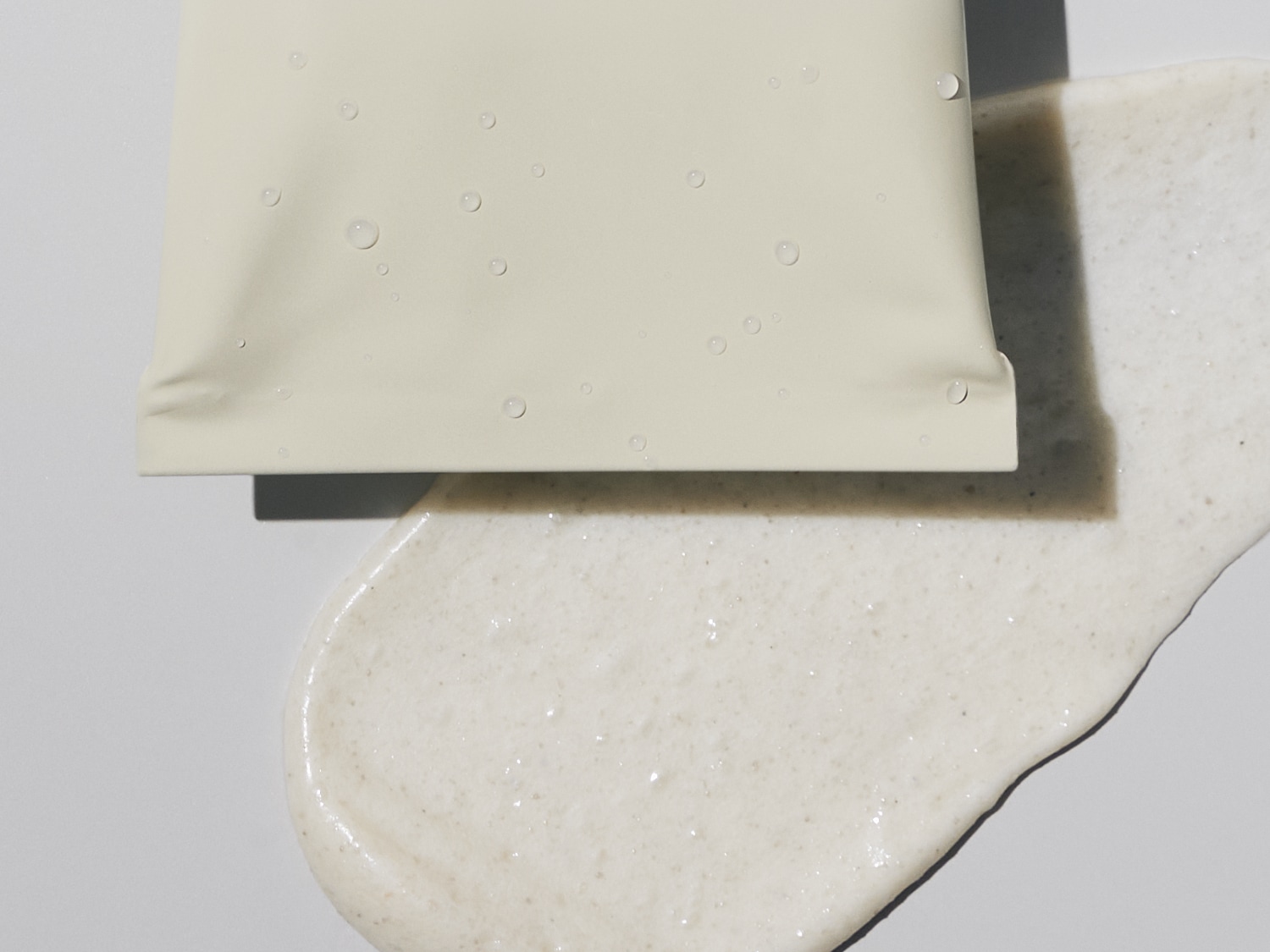 Nahaufnahme einer hellgelben Tube mit Wassertropfen, die auf einer cremigen, hellbraunen Substanz liegt.