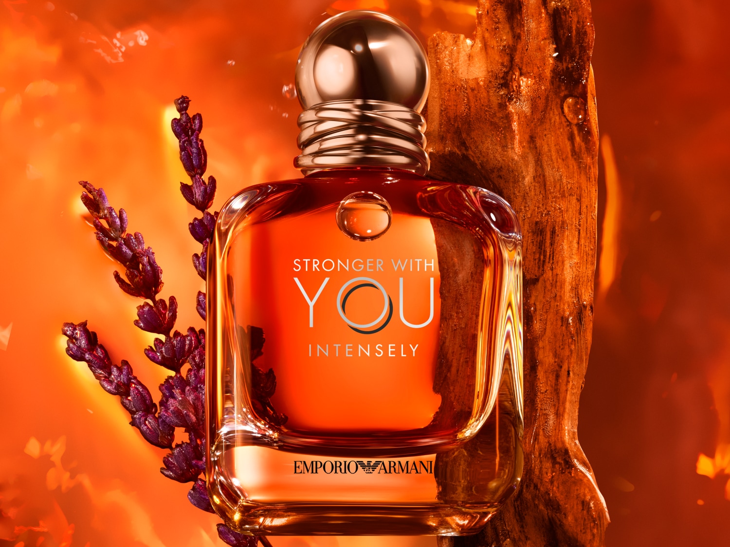 Das Emporio Armani 'Stronger With You Intensely' Eau de Parfum präsentiert sich in einem bernsteinfarbenen Flakon mit goldenem Verschluss, begleitet von Lavendel und einem Stück Holz.