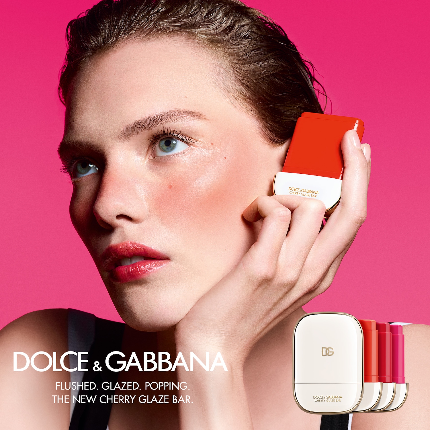 Een vrouw met een rode blos op haar wangen houdt een Dolce & Gabbana Cherry Glaze Bar vast tegen een roze achtergrond, met de tekst: 'FLUSHED. GLAZED. POPPING. THE NEW CHERRY GLAZE BAR.'