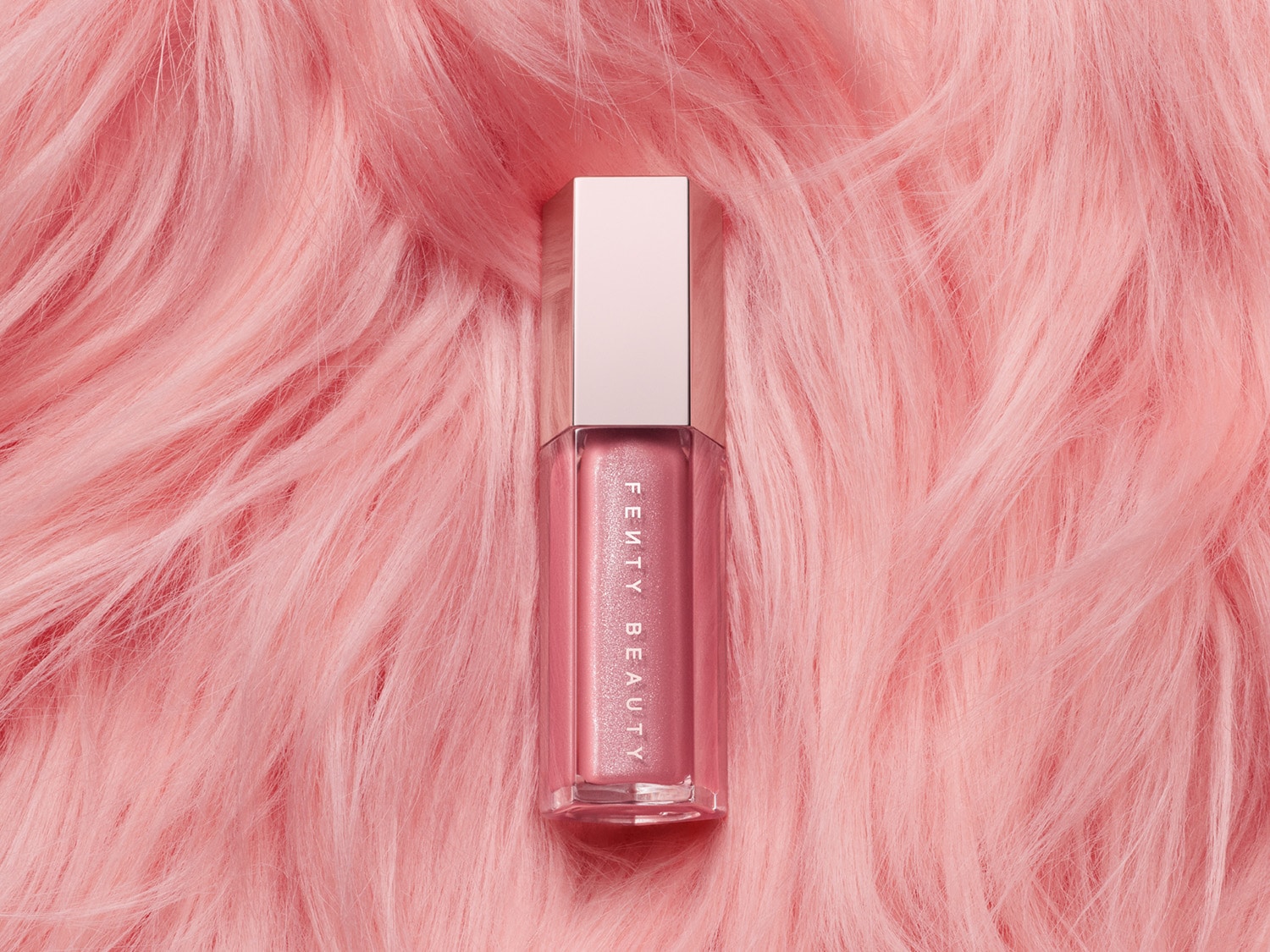 Roze Fenty Beauty lipgloss met glitters, liggend op een zachte, roze ondergrond.