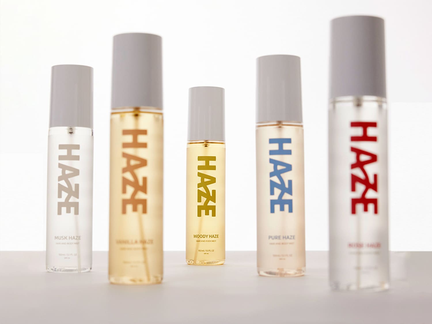 Ontdek de Haze collectie: een reeks haar- en bodymists in diverse geuren, gepresenteerd in strakke, transparante flessen met minimalistische grijze doppen en kleurgecodeerde labels.