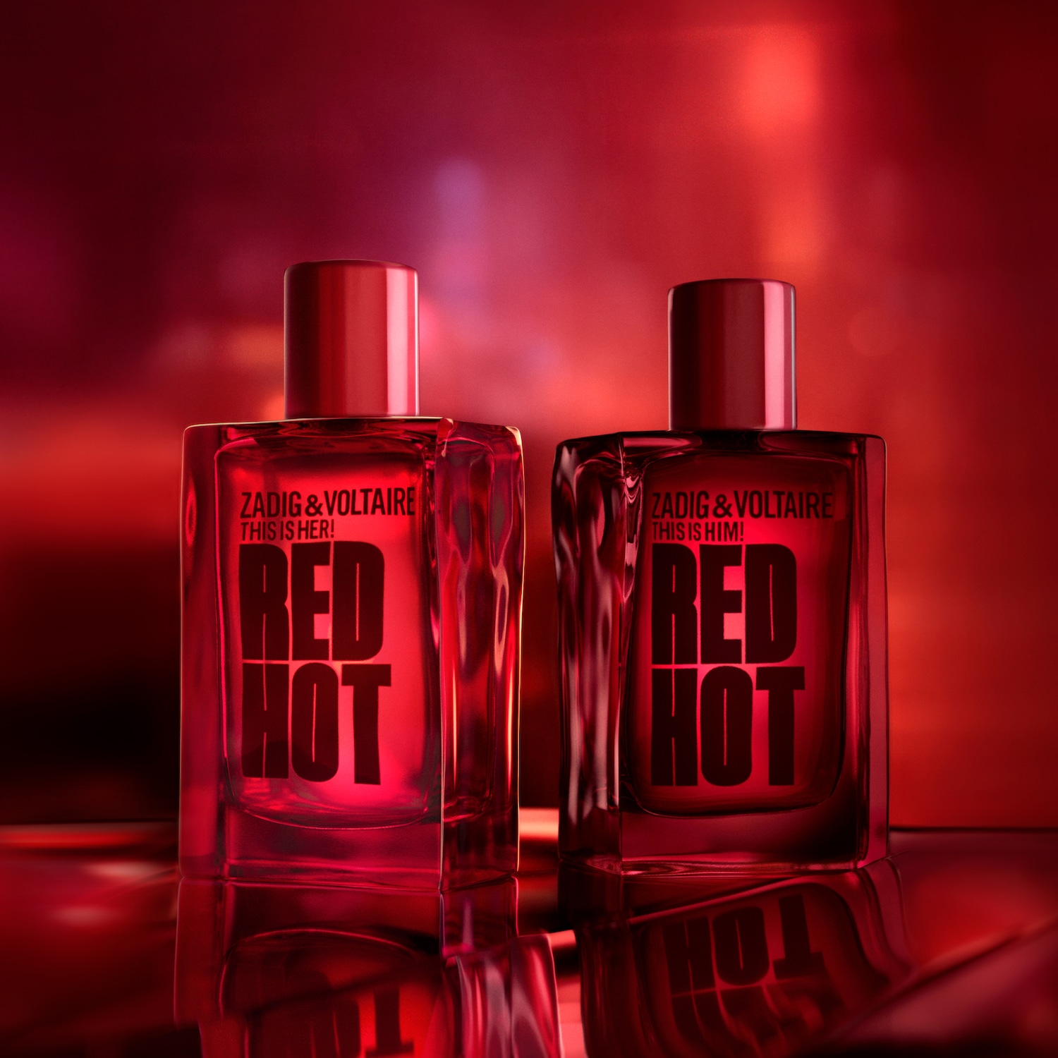 Twee rode parfumflesjes van Zadig & Voltaire, "This is Her! RED HOT" en "This is Him! RED HOT", staan op een glanzend oppervlak tegen een wazige rode achtergrond.