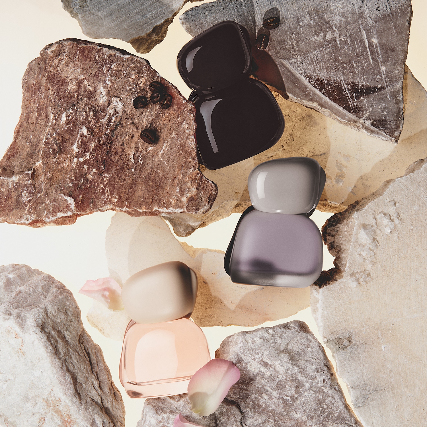 Drie parfumflesjes in de kleuren zwart, lila en perzikroze, omringd door ruwe stenen, koffiebonen en rozenblaadjes, wat een natuurlijke en luxueuze uitstraling geeft.