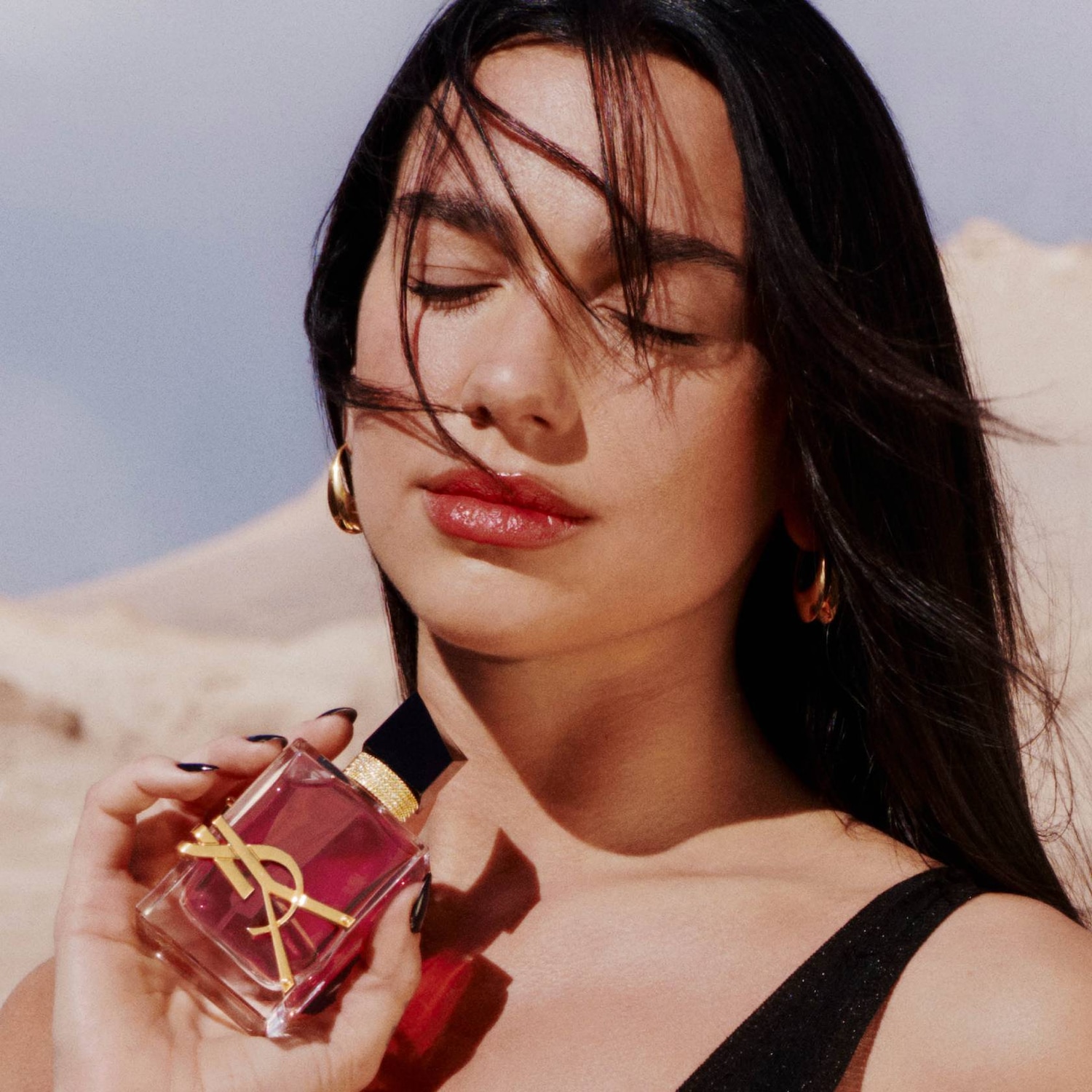 Een vrouw met gesloten ogen houdt een vierkante fles YSL Libre Eau de Parfum vast, met een gouden logo en een zwarte dop, tegen een zachte achtergrond.
