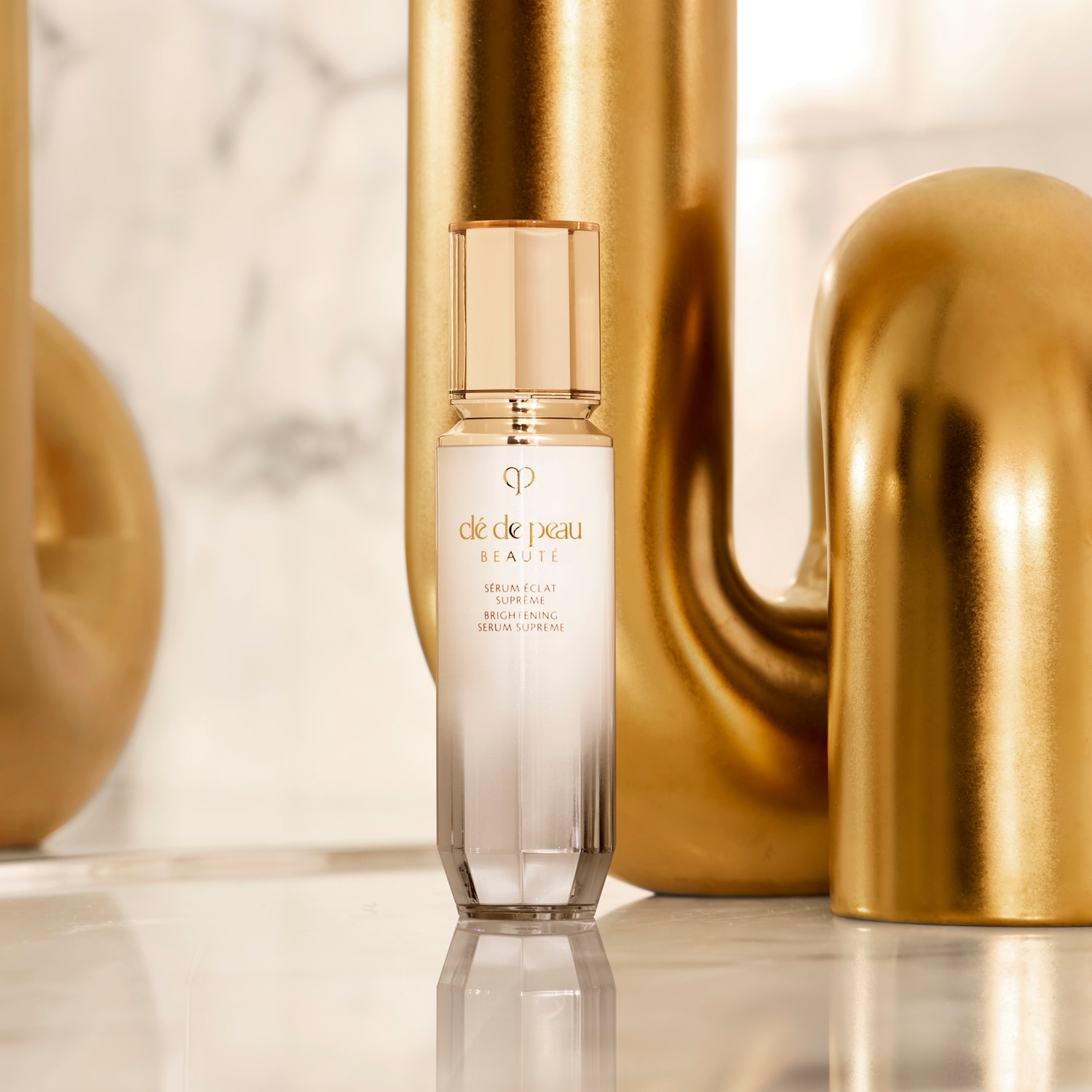 De Clé de Peau Beauté Sérum Éclat Suprême in een elegante witte flacon met gouden accenten, belooft een heldere en stralende huid.