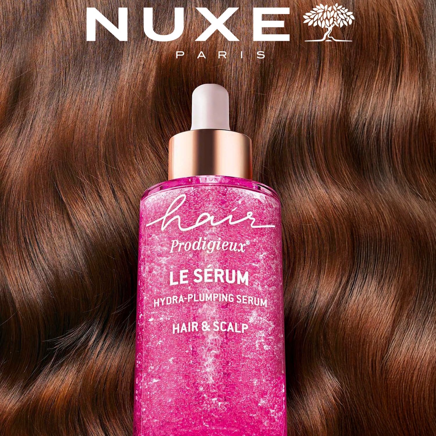 Nuxe Paris Hair Prodigieux Le Serum Hydra-Plumping Serum voor haar en hoofdhuid, gepresenteerd in een roze fles met een gouden dop, tegen een achtergrond van golvend bruin haar.