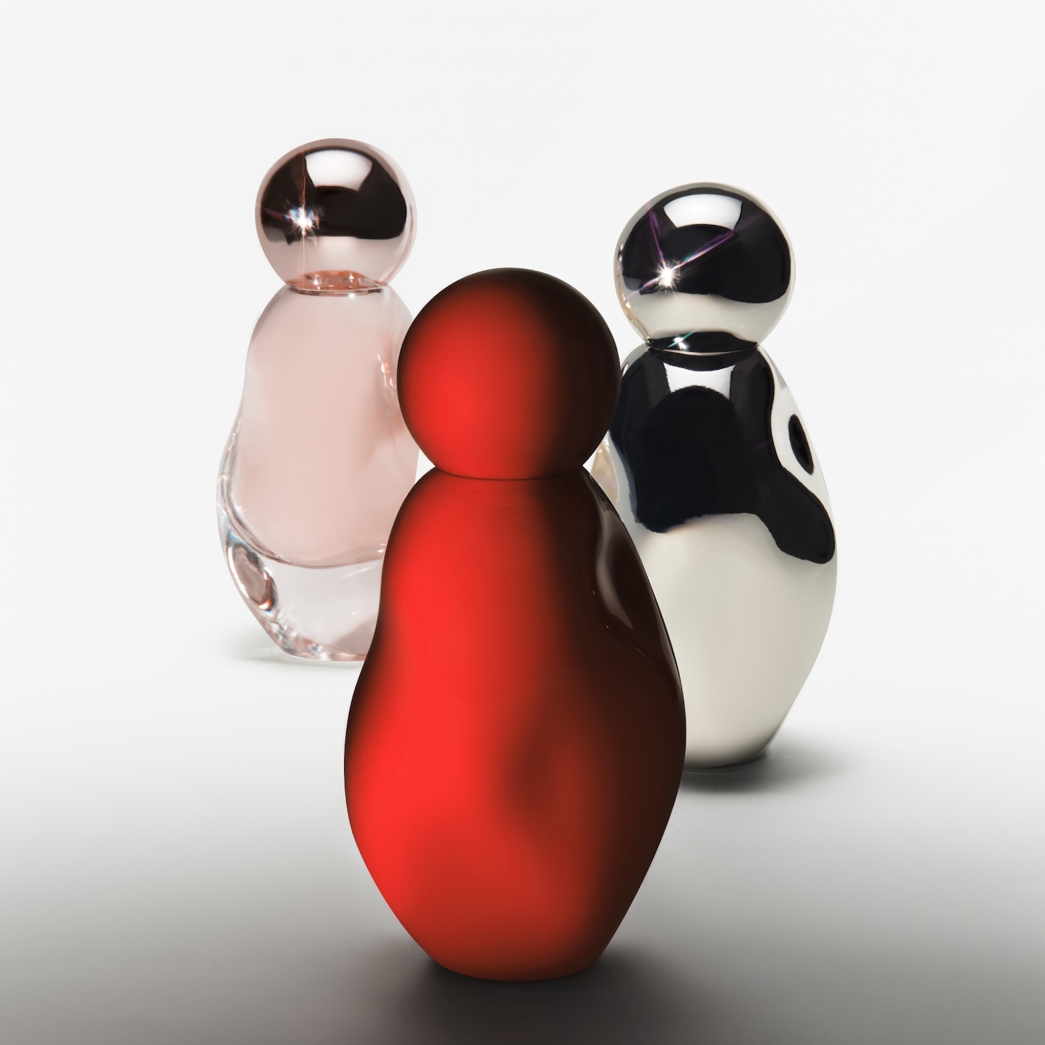 Drie flessen in de vorm van een kegel met een bol erop, de eerste is rood, de tweede is roze en de derde is zwart en wit.