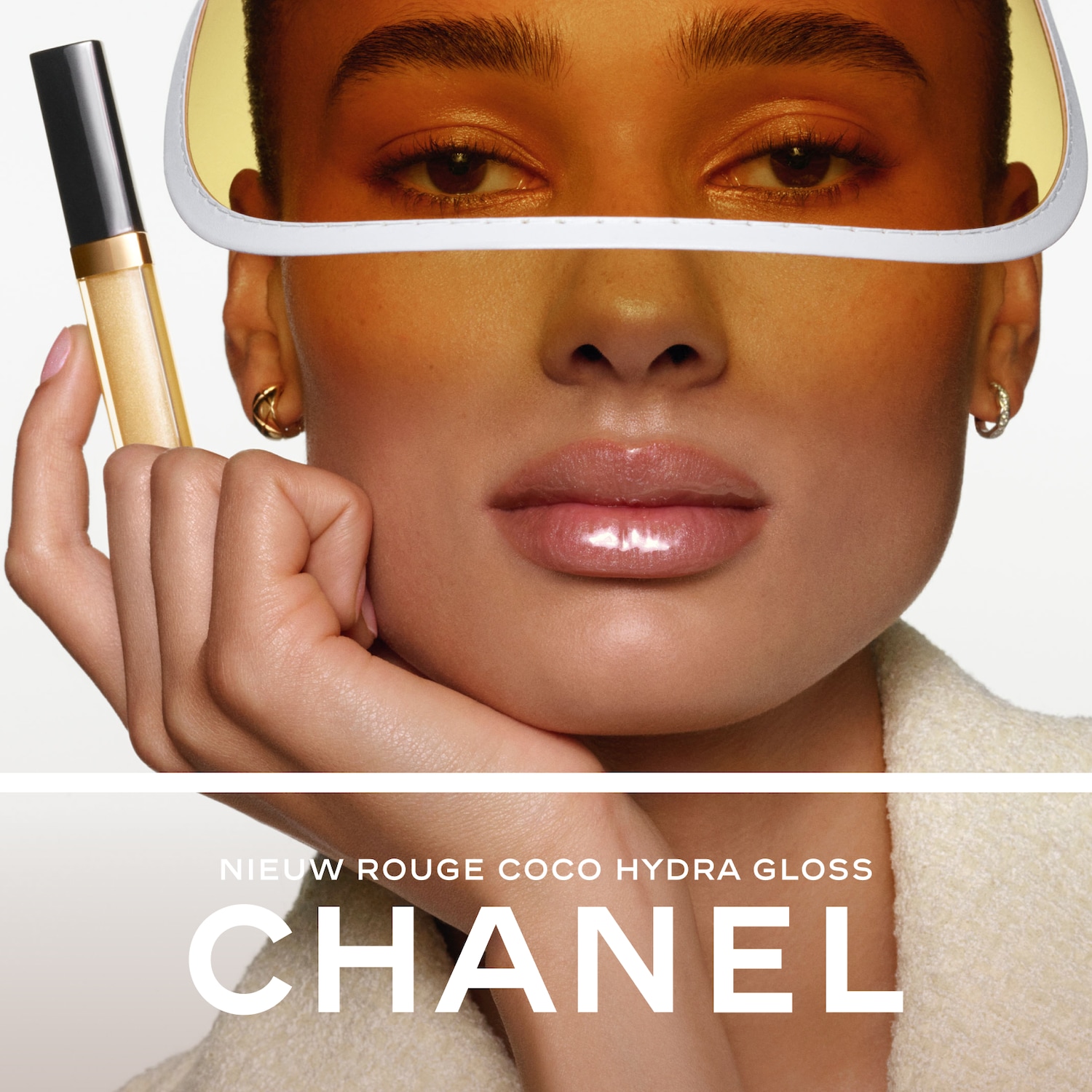 Een vrouw met een glanzende lipgloss en een geel vizier houdt een Chanel Rouge Coco Hydra Gloss vast, met de tekst "NIEUW ROUGE COCO HYDRA GLOSS CHANEL" eronder.