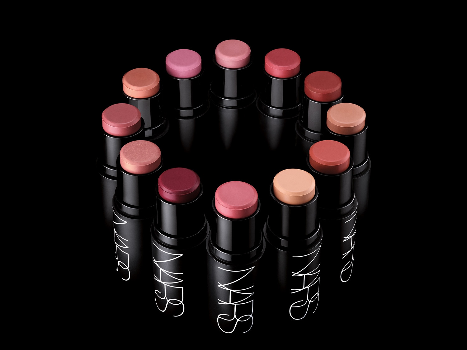 Een cirkel van NARS blush sticks in verschillende tinten, van roze tot perzik, allemaal verpakt in strakke, zwarte hulzen met het witte NARS logo.