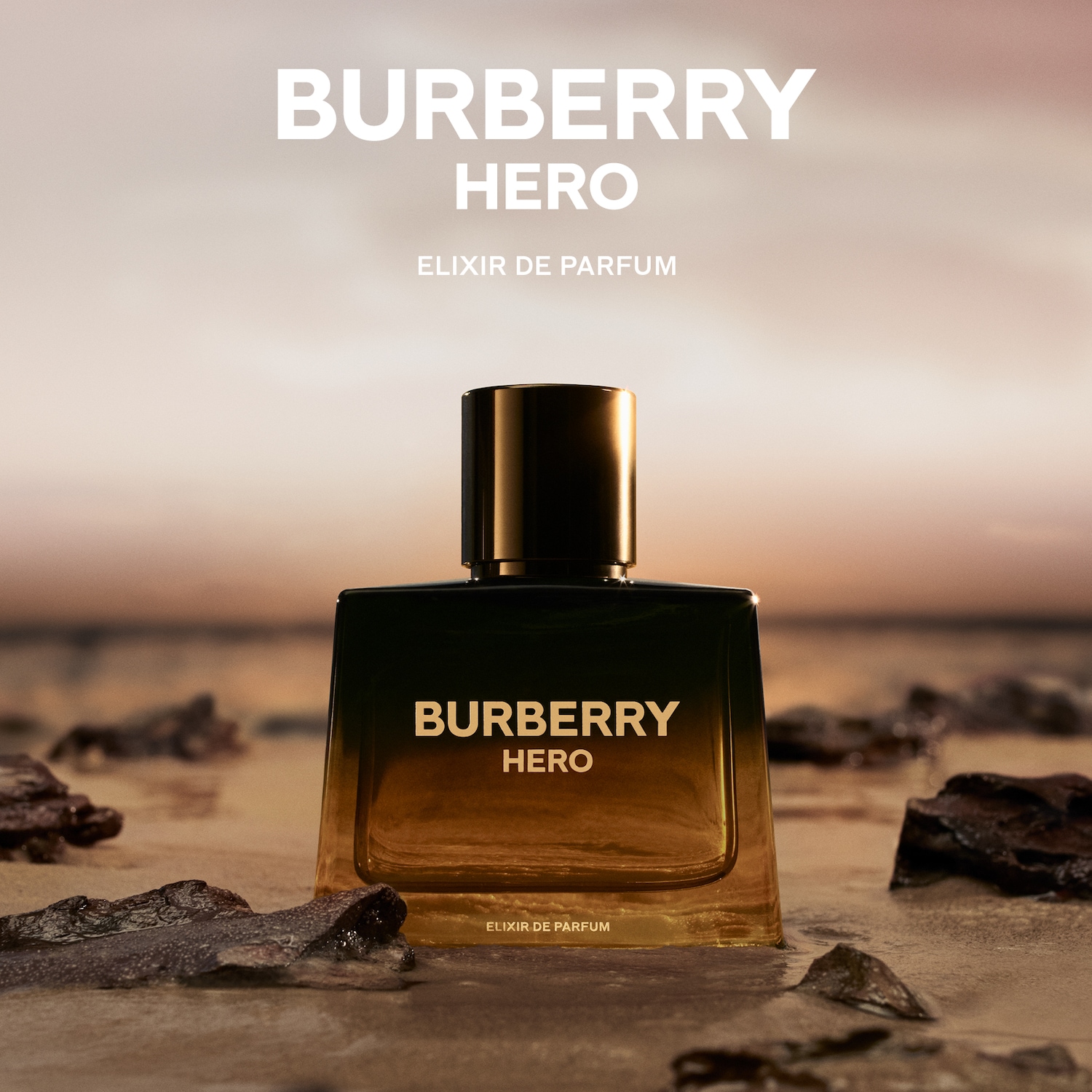 Burberry Hero Elixir de Parfum, een amberkleurige vloeistof in een donkergroene flacon met de merknaam erop, staat op een zandstrand.