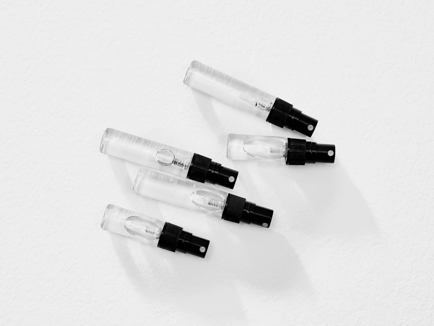 Nahaufnahme von fünf durchsichtigen Parfümproben mit schwarzen Sprühköpfen, die auf einer weißen Oberfläche liegen.