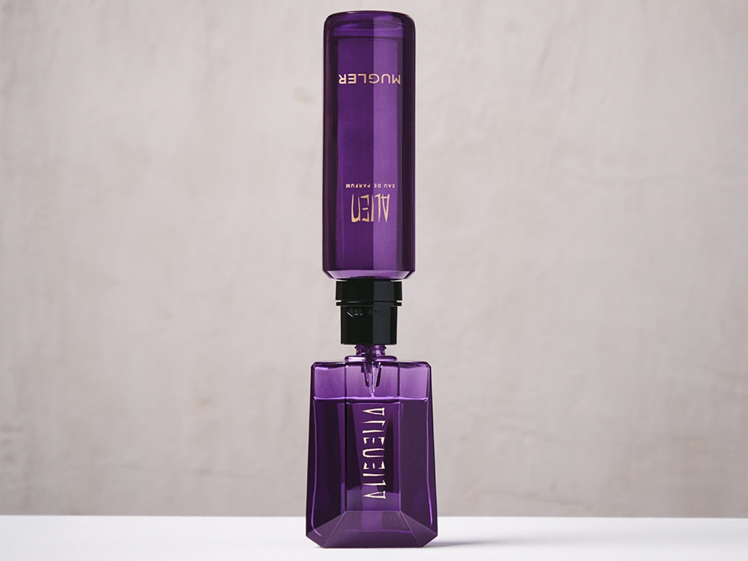 Un flacon de parfum violet Mugler Alien Eau de Parfum est rechargé par une recharge violette, les deux flacons étant alignés verticalement sur un fond blanc.