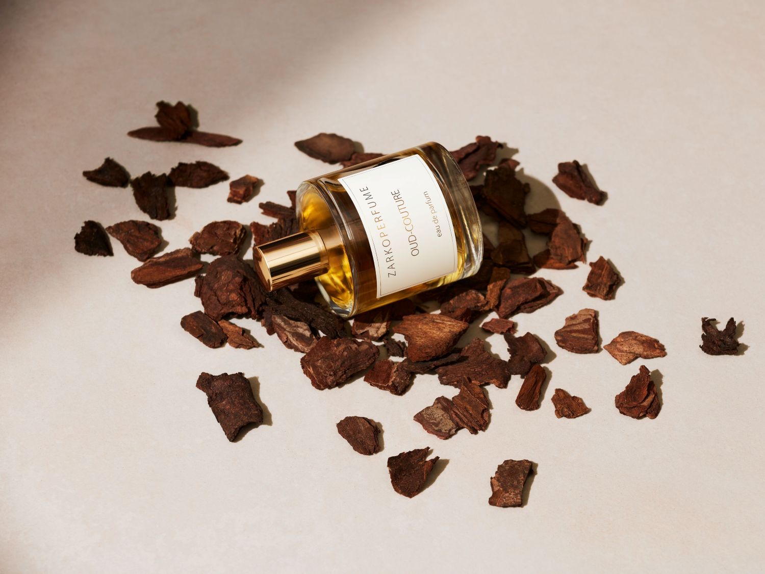 Lahvička parfému ZARKOPERFUME Oud-Couture leží na kouscích kůry, má zlatý uzávěr a průhlednou tekutinu.