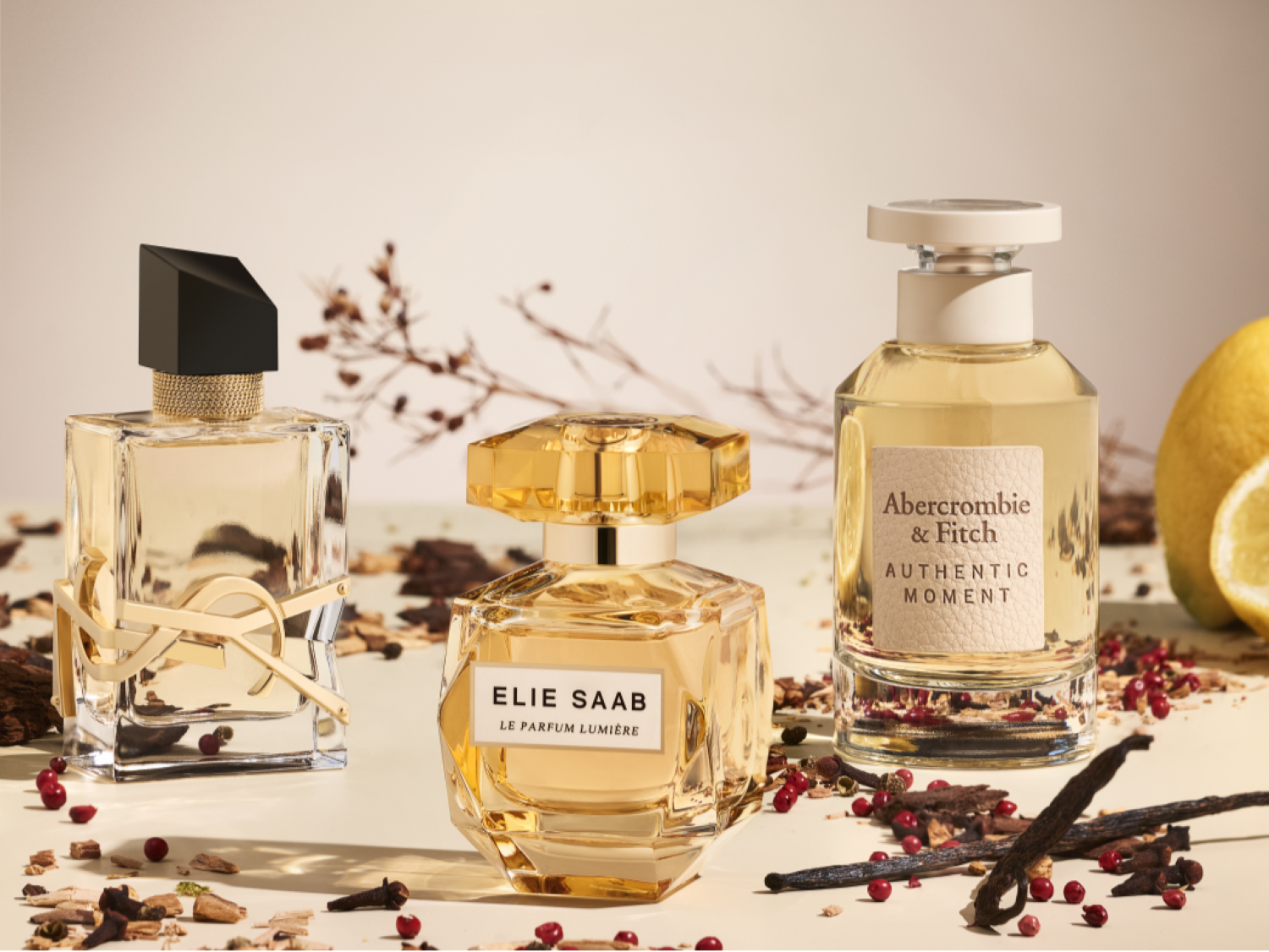 Tři flakony parfémů různých značek, YSL, Elie Saab a Abercrombie & Fitch, v teplých tónech s dřevitými a citrusovými akcenty.