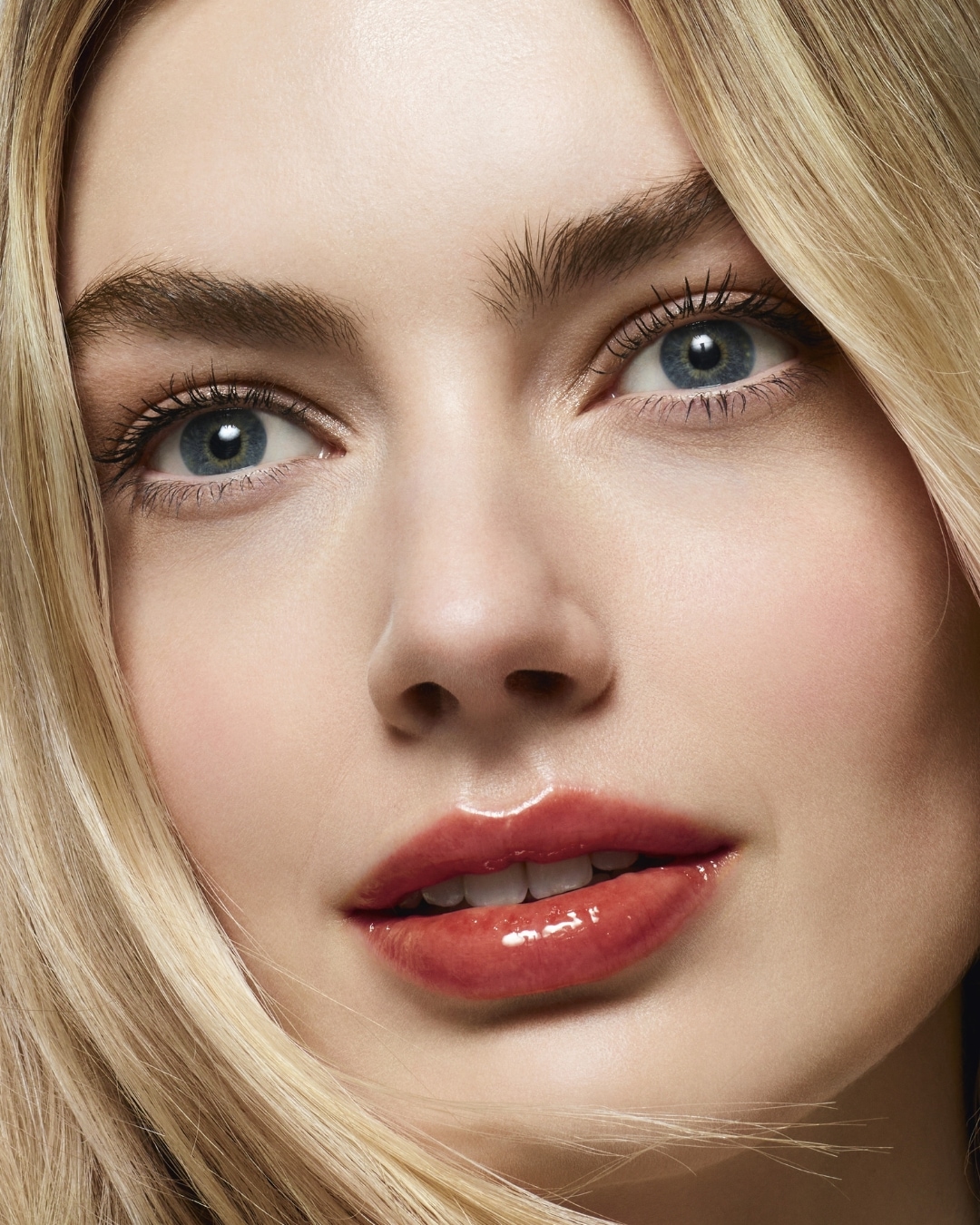 Acércate a la belleza con una mirada que destaca gracias a los ojos azules y los labios brillantes con un toque de color coral.