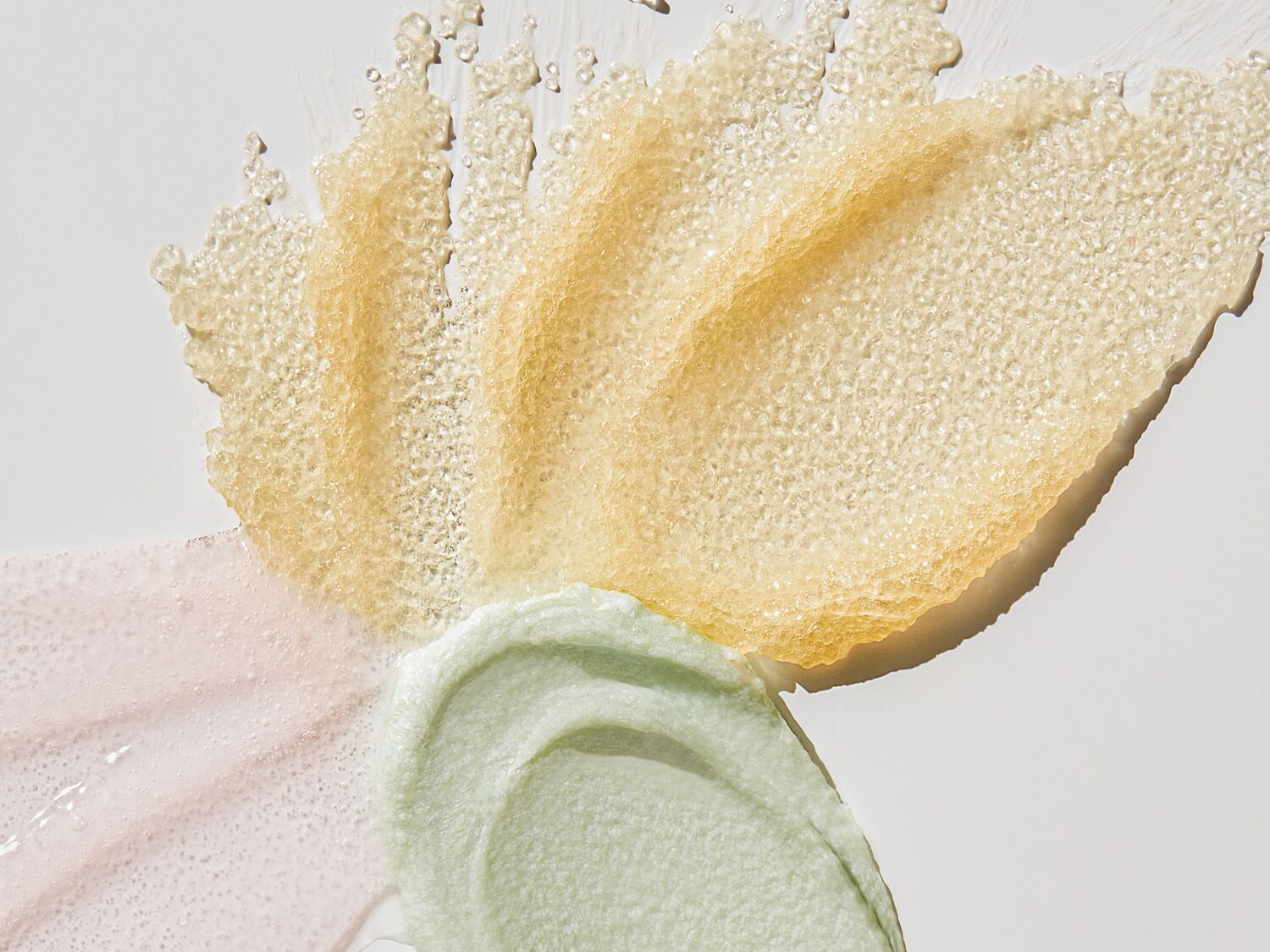 Štai geltonos, žalios ir rožinės spalvos kosmetikos priemonės tepinėliai, skirti odos priežiūrai.