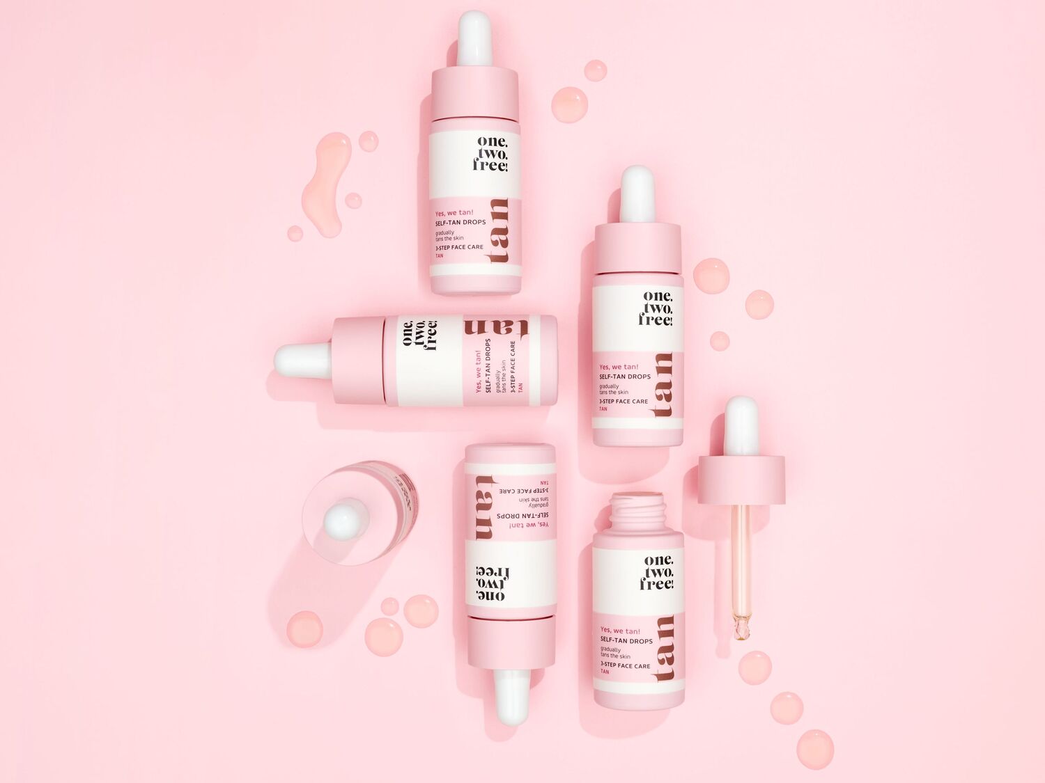 Rožiniame fone išdėstyti „One, Two, Free!“ savaiminio įdegio lašai, skirti palaipsniui įdegti odą ir prižiūrėti veido odą vienu žingsniu.
