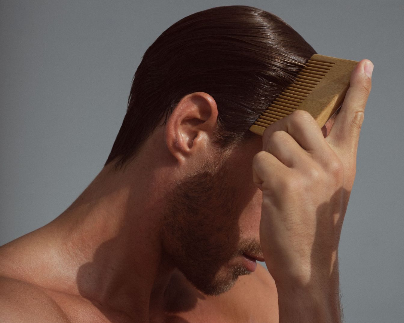 Muž si upravuje svoje lesklé, tmavé vlasy dreveným hrebeňom, čím demonštruje starostlivosť o vlasy a osobnú úpravu.