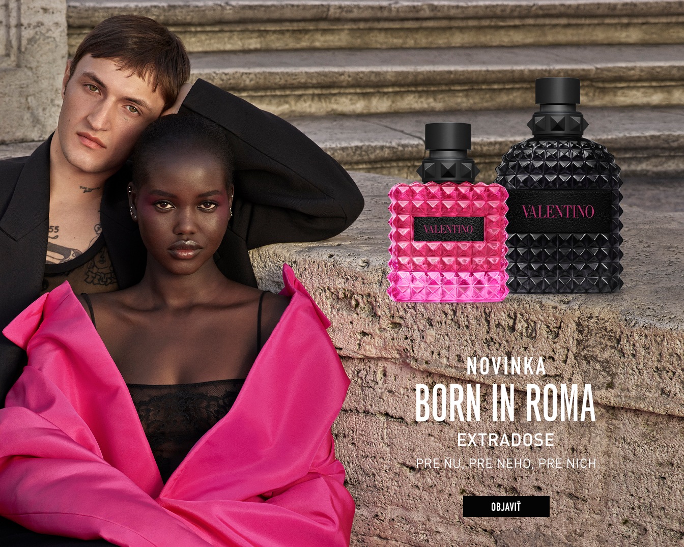 A Valentino Born in Roma Extradose parfümök rózsaszín és fekete, szegecses üvegben láthatók egy pár mellett, a "Born in Roma" felirattal, fedezd fel most.