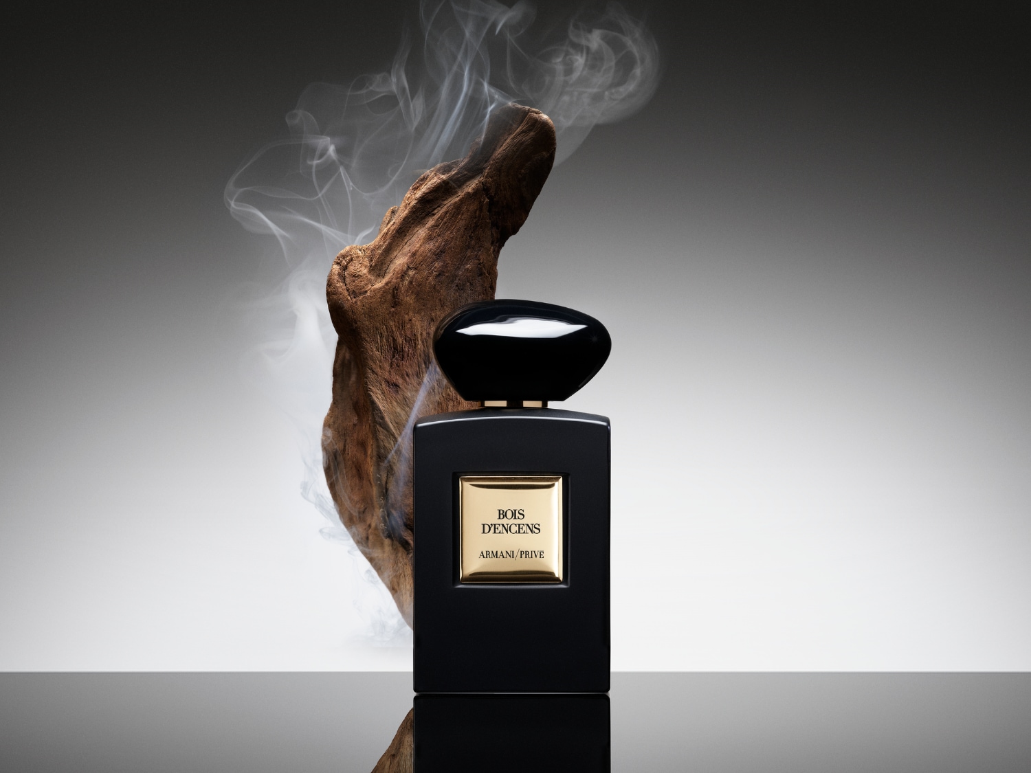 A Bois D'Encens Armani Privé parfümös üveg egy faág mellett látható, füsttel körülvéve, ami egy titokzatos és fás illatot sugall.