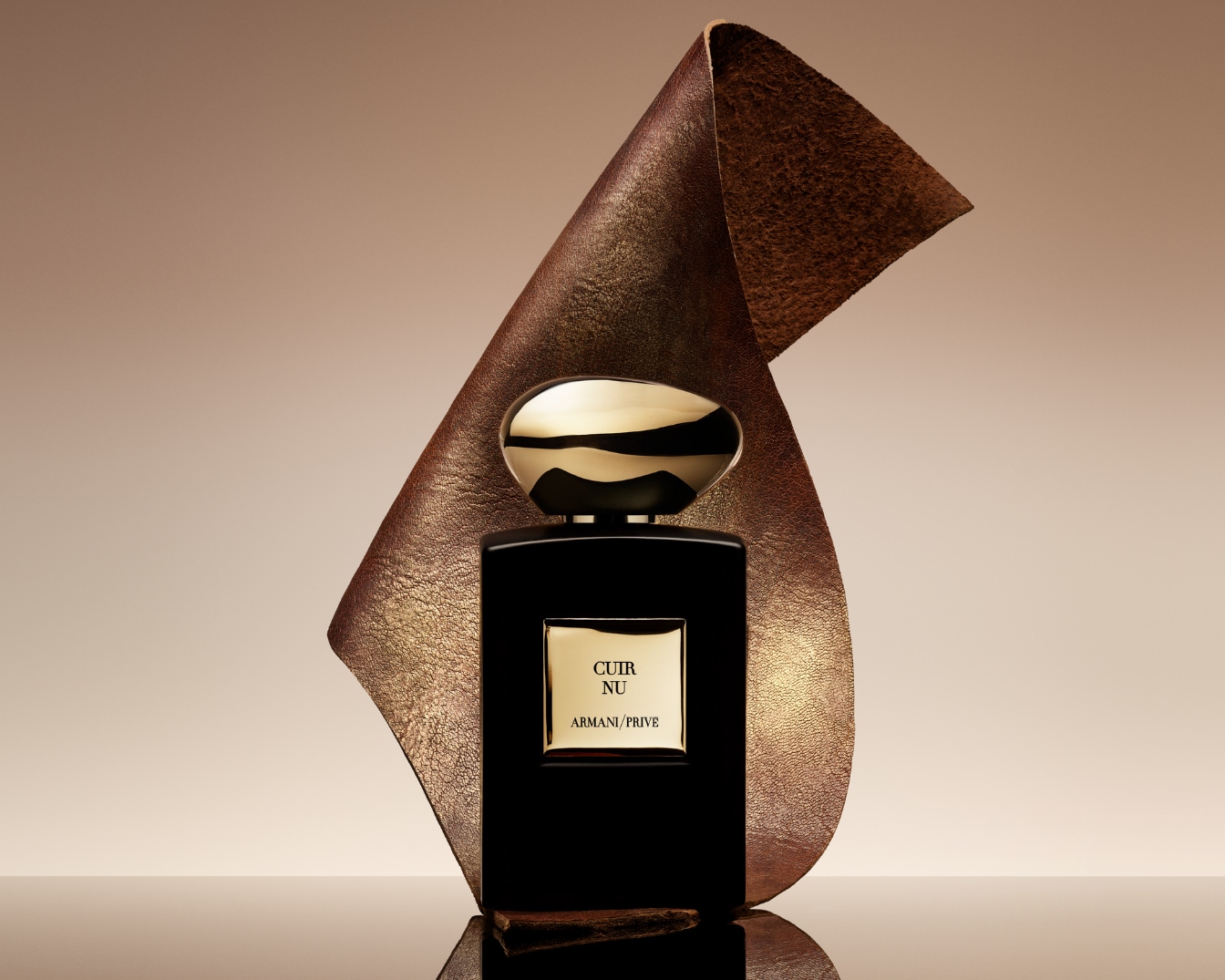 A Cuir Nu Armani Prive parfüm fekete üvegben, arany kupakkal és címkével, egy texturált barna bőr darab mögött áll, elegáns és kifinomult megjelenést kölcsönözve.