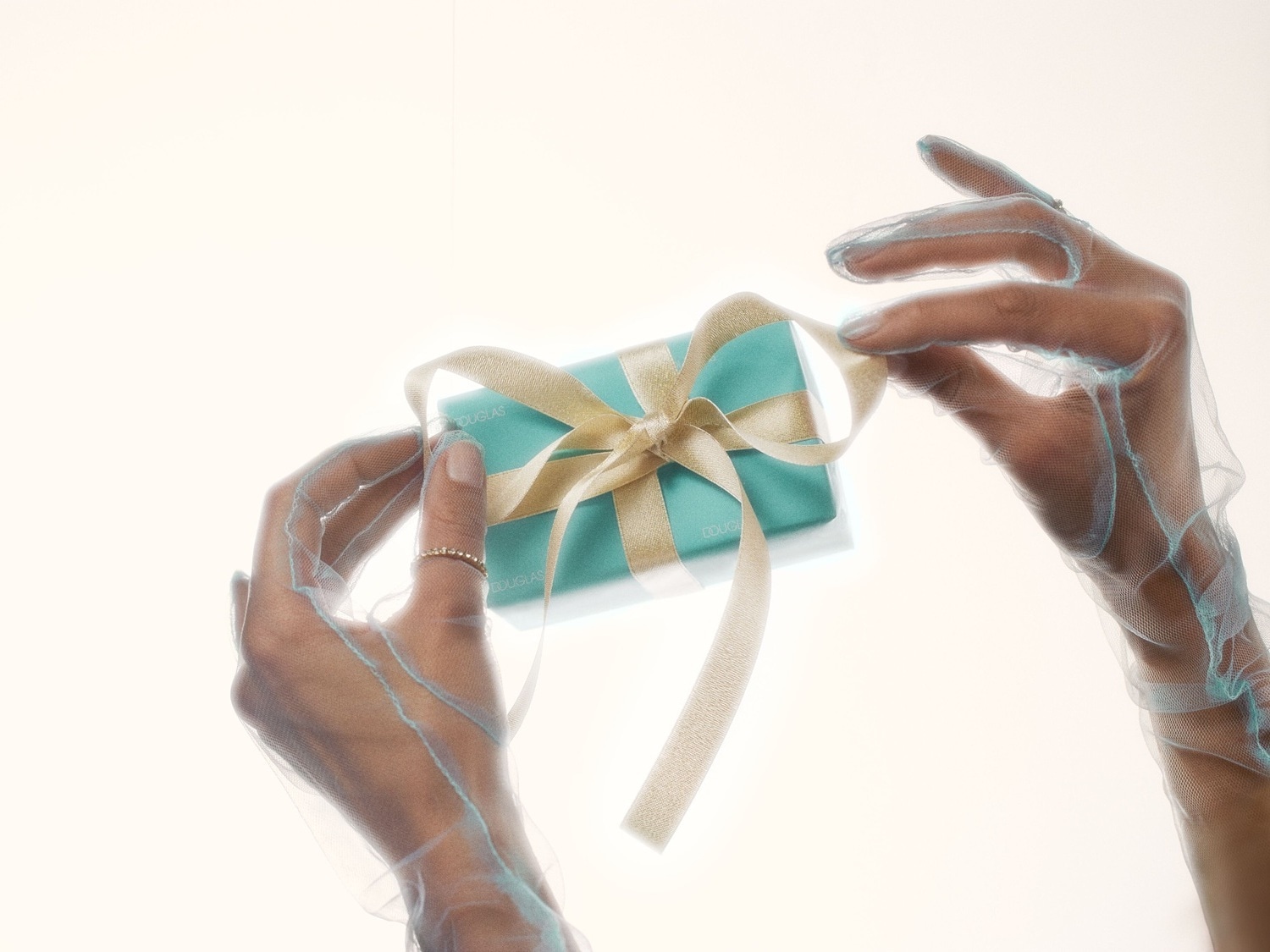 A stack of turquoise Douglas gift boxes tied with a shimmering gold ribbon, creating a festive tower against a matching backdrop.