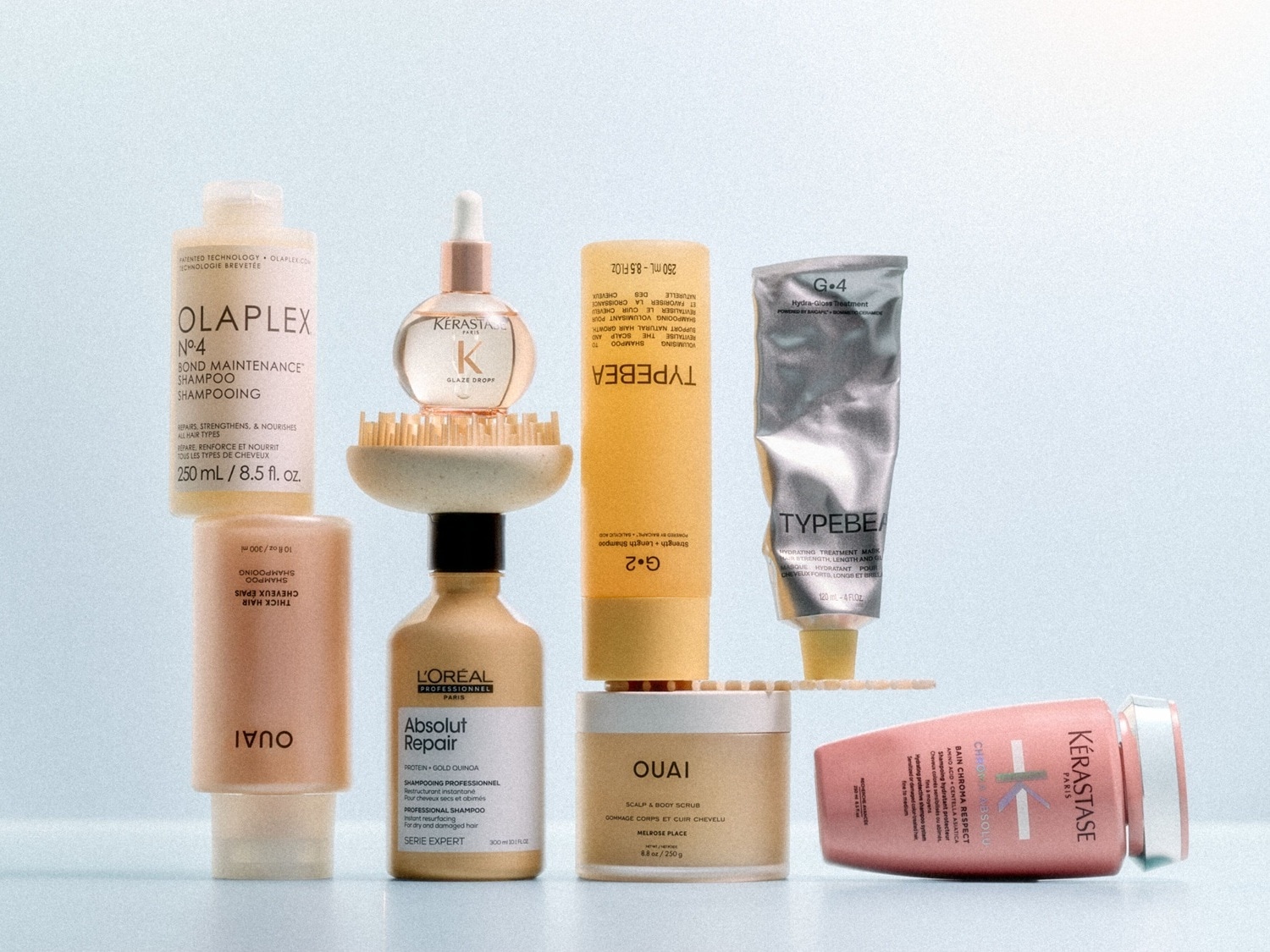 Eine Auswahl an Haarpflegeprodukten, darunter Olaplex Shampoo, Kerastase Glaze Drops, Loreal Absolut Repair Shampoo, Ouai Kopfhaut- und Körperpeeling und Typebea Haarpflege, die alle Haartypen reparieren, stärken und pflegen.