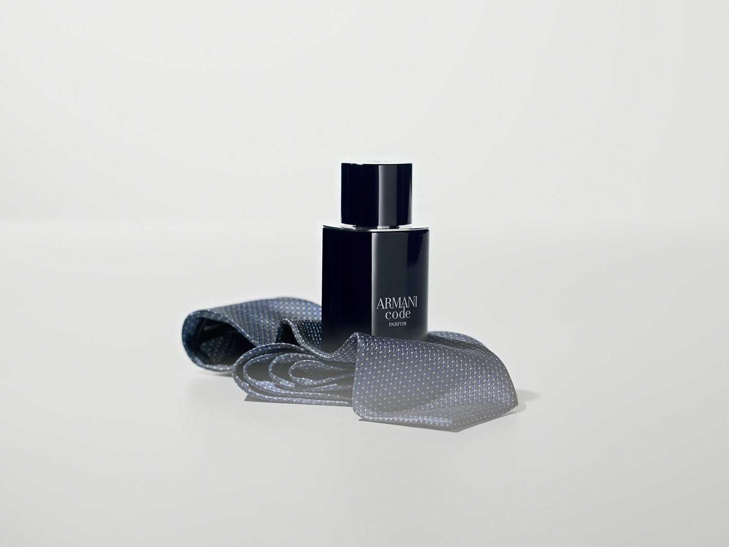 Eine dunkle Armani Code Parfum Flasche steht auf einer grauen Krawatte mit Punktmuster.