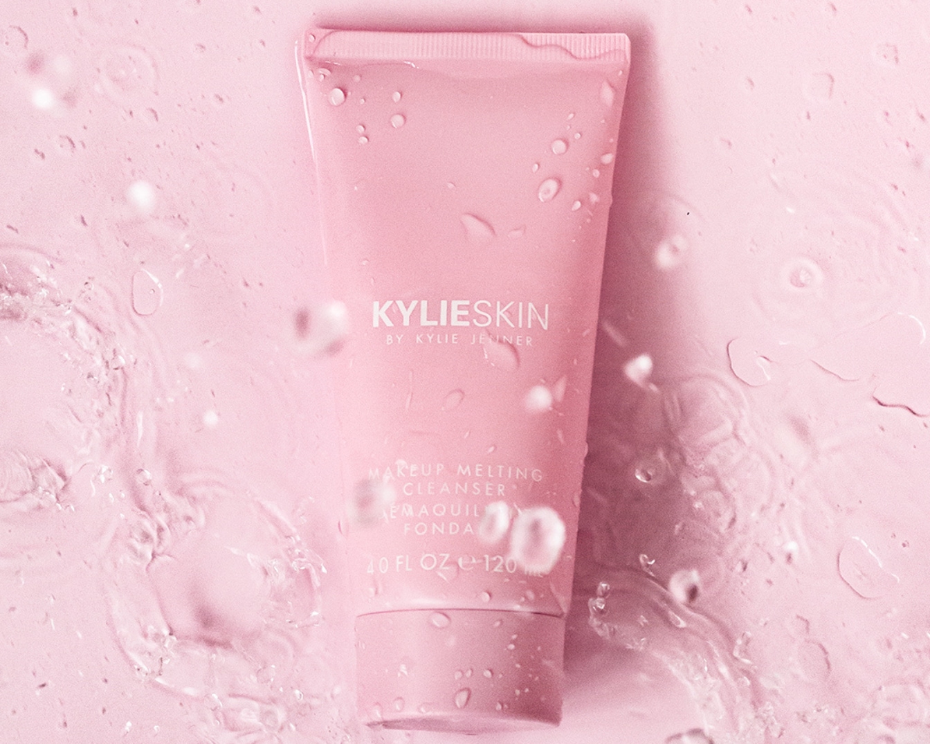 Roze tube Kylie Skin Makeup Melting Cleanser, omringd door waterdruppels, belooft een zachte reiniging voor een stralende huid.