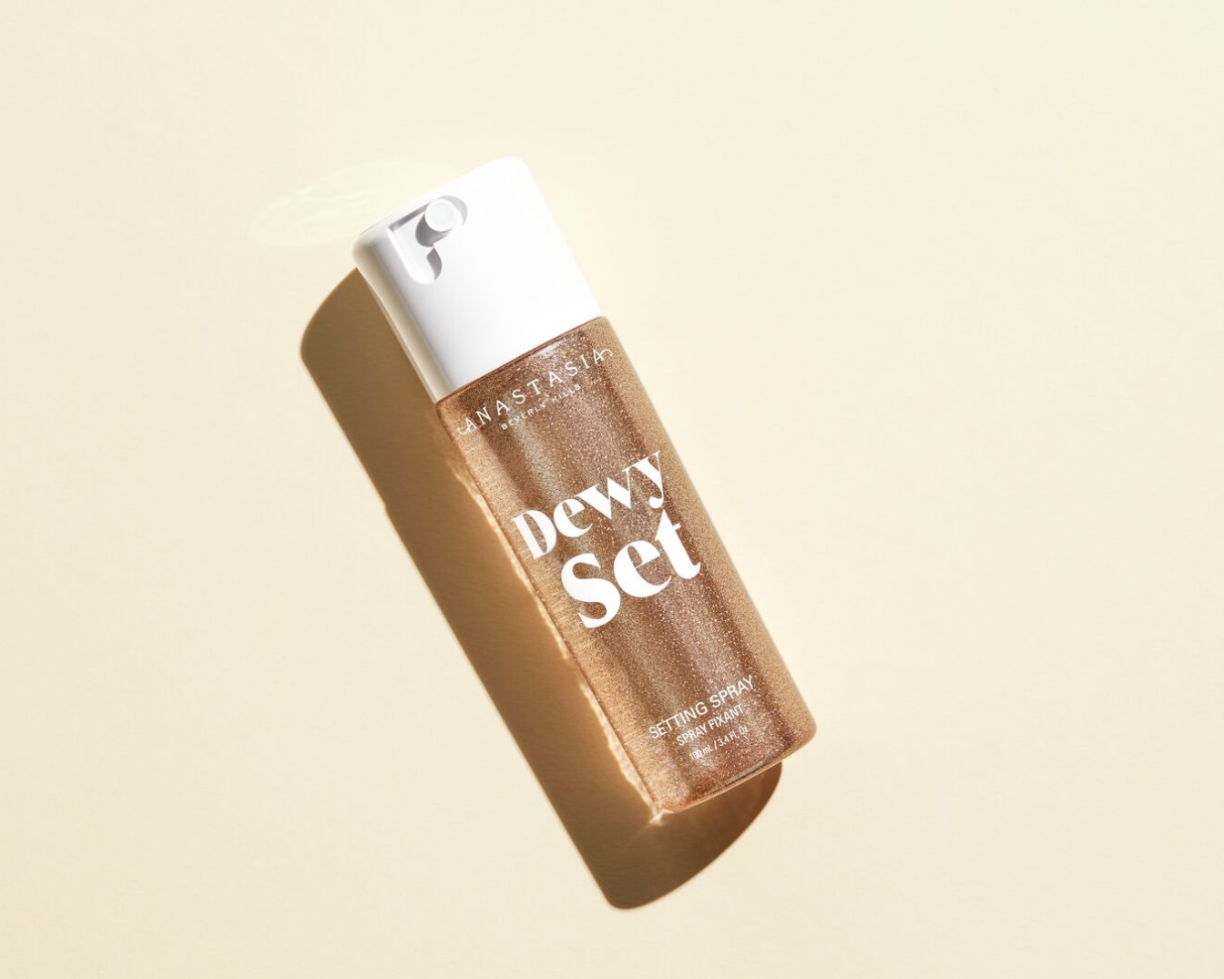 Gouden Anastasia Beverly Hills 'Dewy Set' setting spray in een doorzichtige flacon met witte dop, klaar om je make-up een stralende finish te geven.