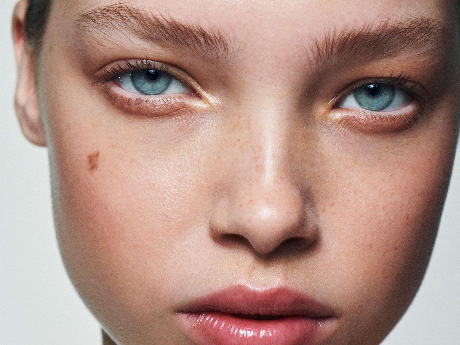 Nahaufnahme eines jungen Gesichts mit hellblauen Augen, Sommersprossen und vollen, glänzenden Lippen.