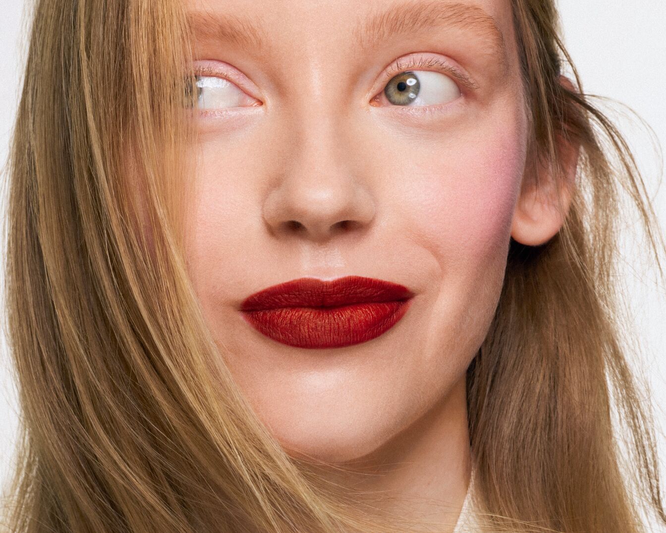 Nahaufnahme eines Frauengesichts mit roten Lippen, rosigen Wangen und blonden Haaren, die zur Seite blickt.