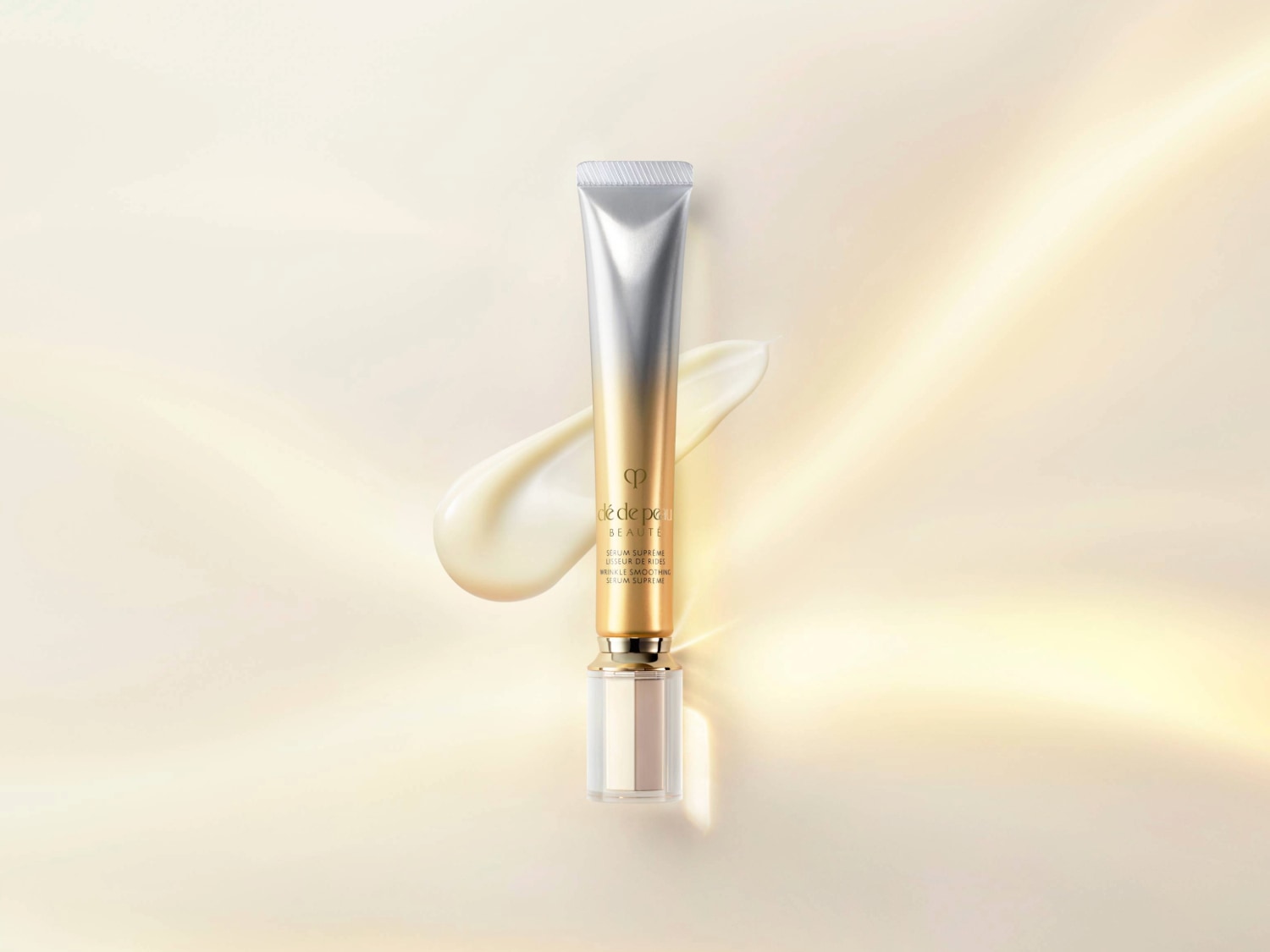 Voici un tube de sérum de beauté Clé de Peau, argenté en haut et doré en bas, avec une touche de crème claire à côté, promettant un lissage suprême des rides.