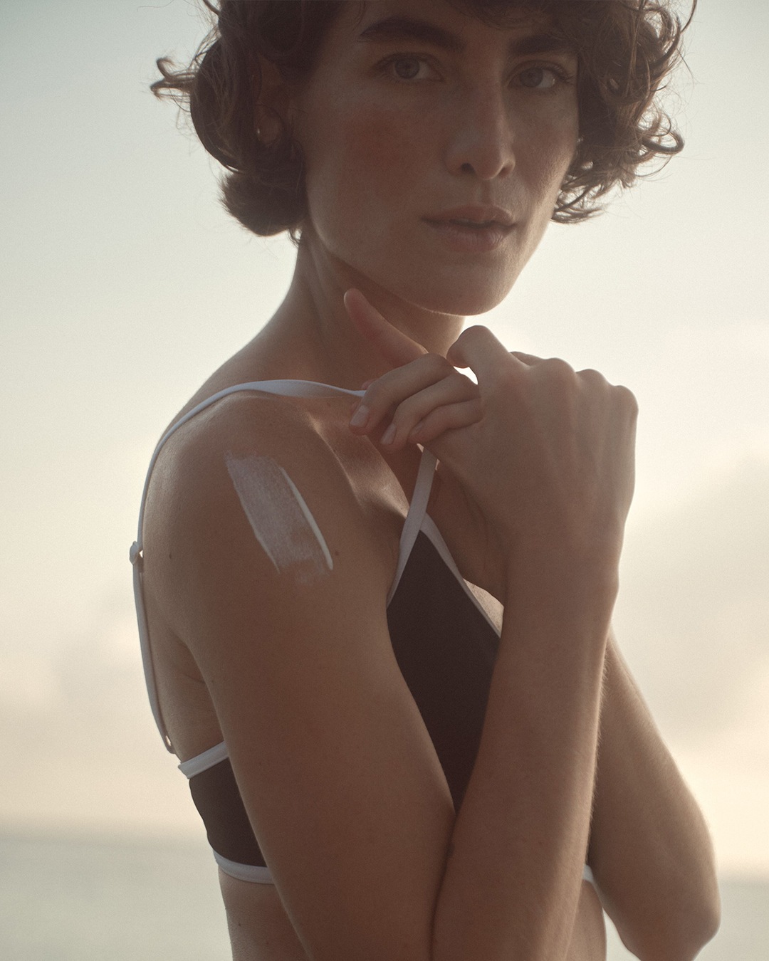 Une femme applique une crème solaire blanche sur son épaule, assurant une protection contre les rayons du soleil.