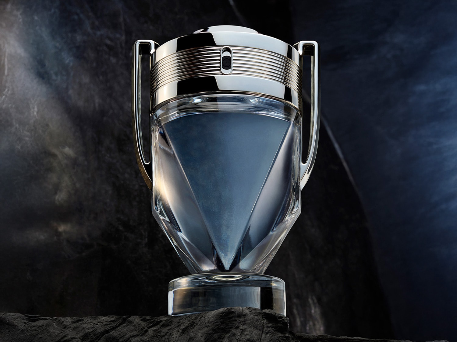 Le parfum Invictus de Paco Rabanne, présenté dans un flacon en forme de trophée argenté et transparent, évoquant la victoire et la fraîcheur.