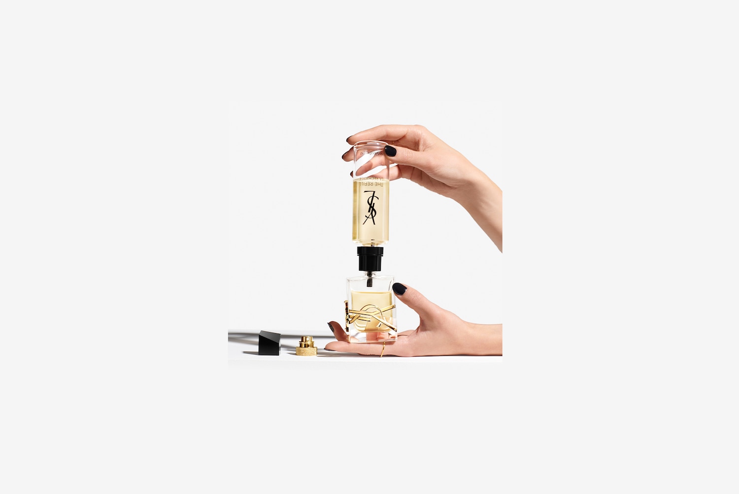 Eine Person befüllt eine transparente YSL-Parfümflasche mit einer Nachfüllpackung, wobei die goldene Flüssigkeit und das ikonische Logo zur Geltung kommen.