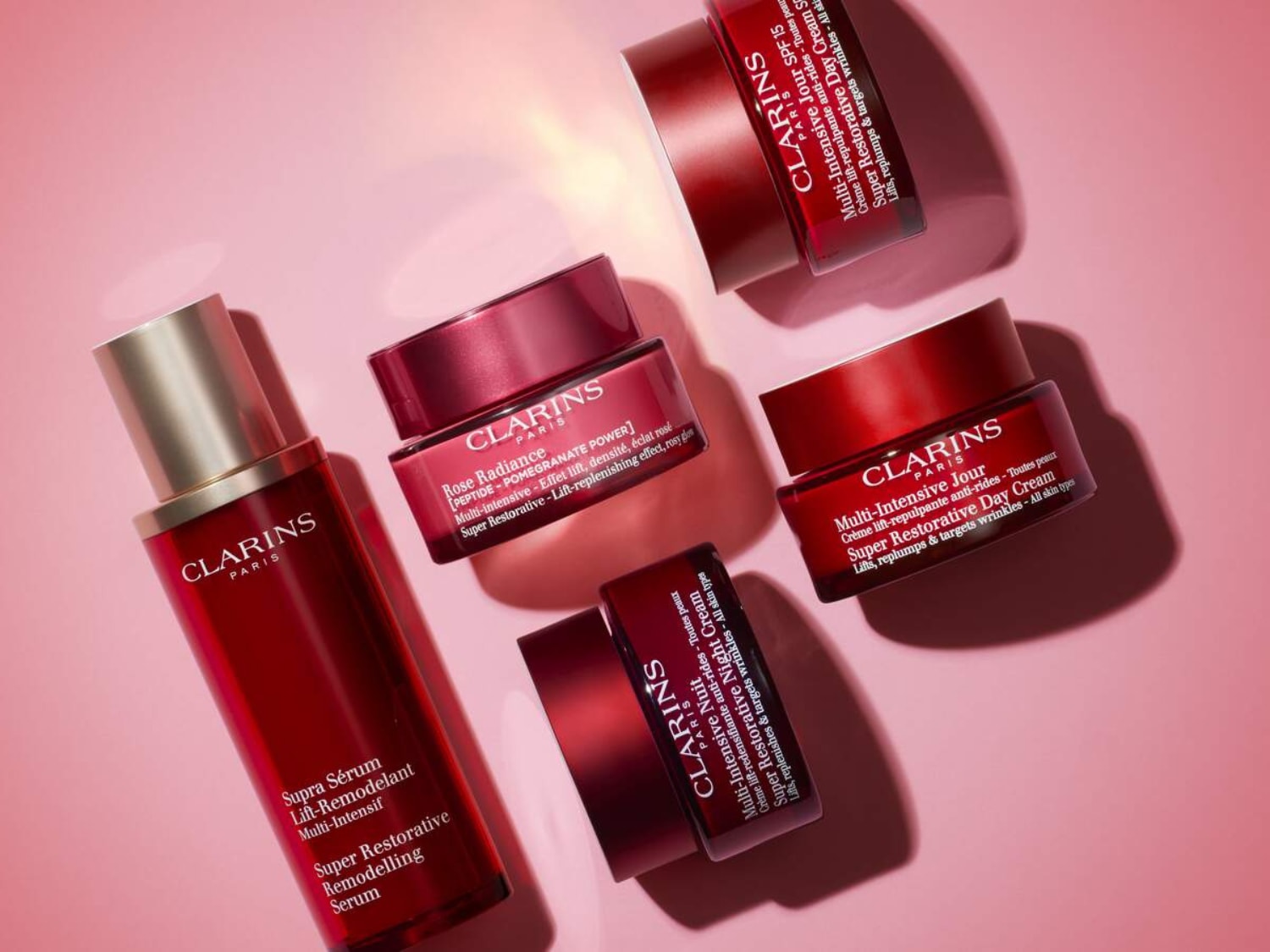 Découvrez la collection Super Restorative de Clarins, comprenant le sérum lift-remodelant, la crème de jour et la crème de nuit, présentés dans des emballages rouge rubis élégants.
