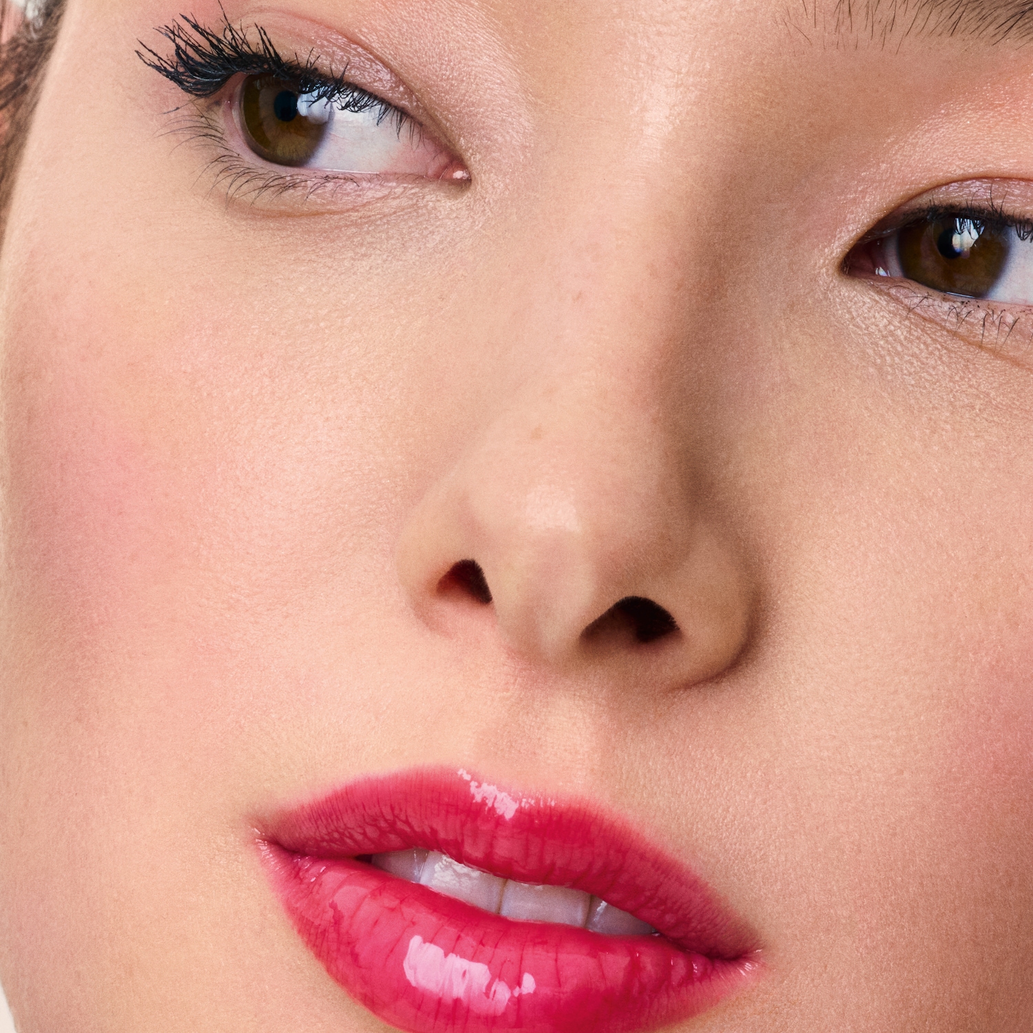 Close-up van een vrouw met een glanzende, felroze lipgloss, bruine ogen met zwarte mascara en een heldere huid.