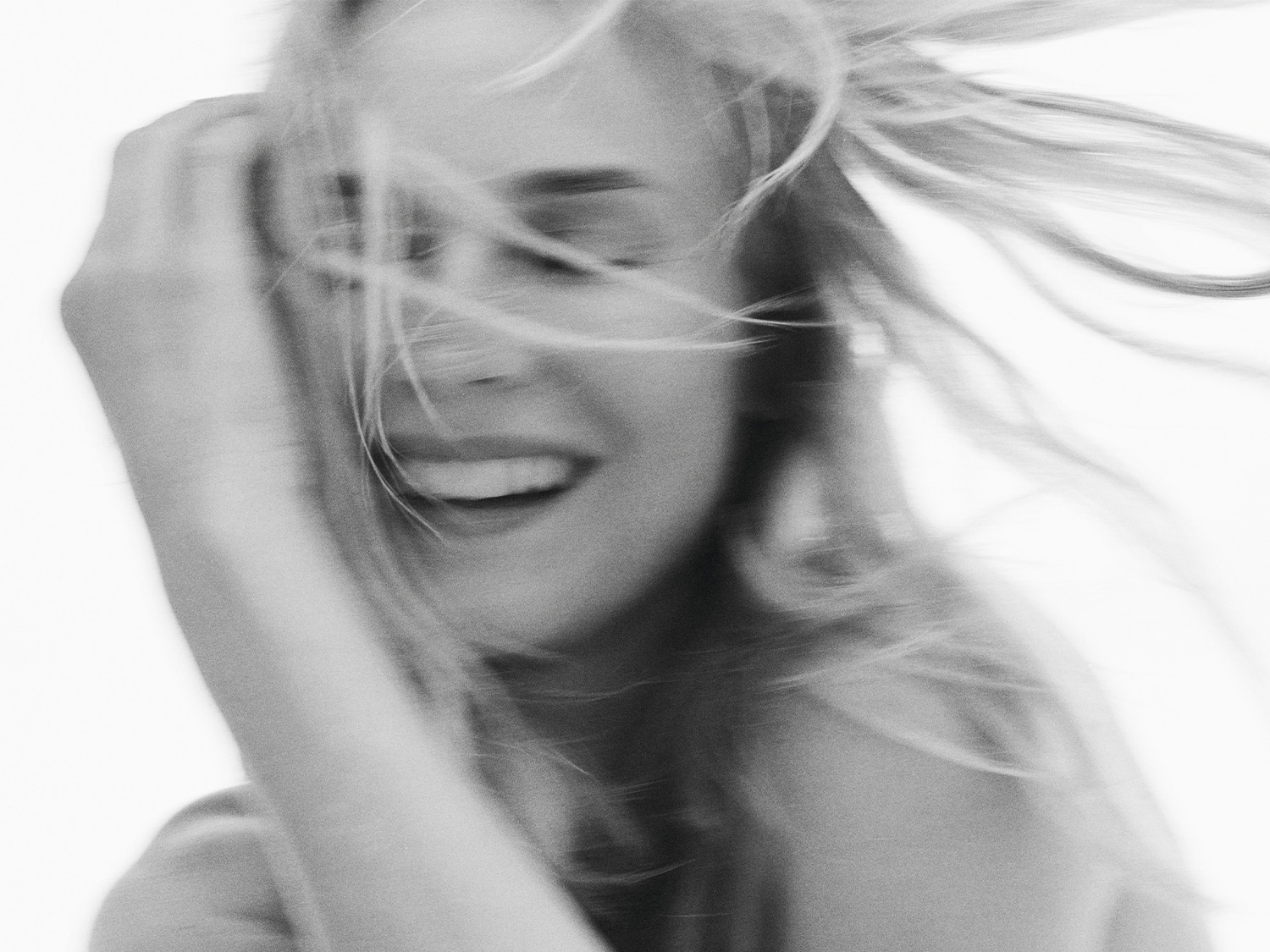 Juodai balta nuotrauka, kurioje matyti besišypsanti moteris, o jos plaukai vėjyje.