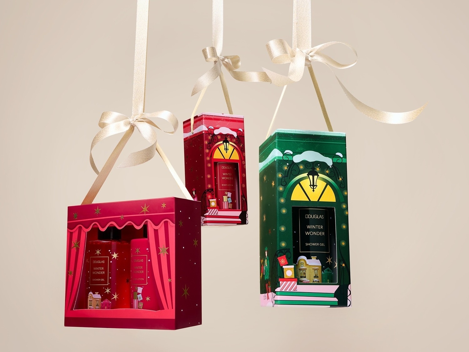Tri darčekové sady Douglas Winter Wonder v červenom a zelenom balení, zavesené na saténových stuhách.