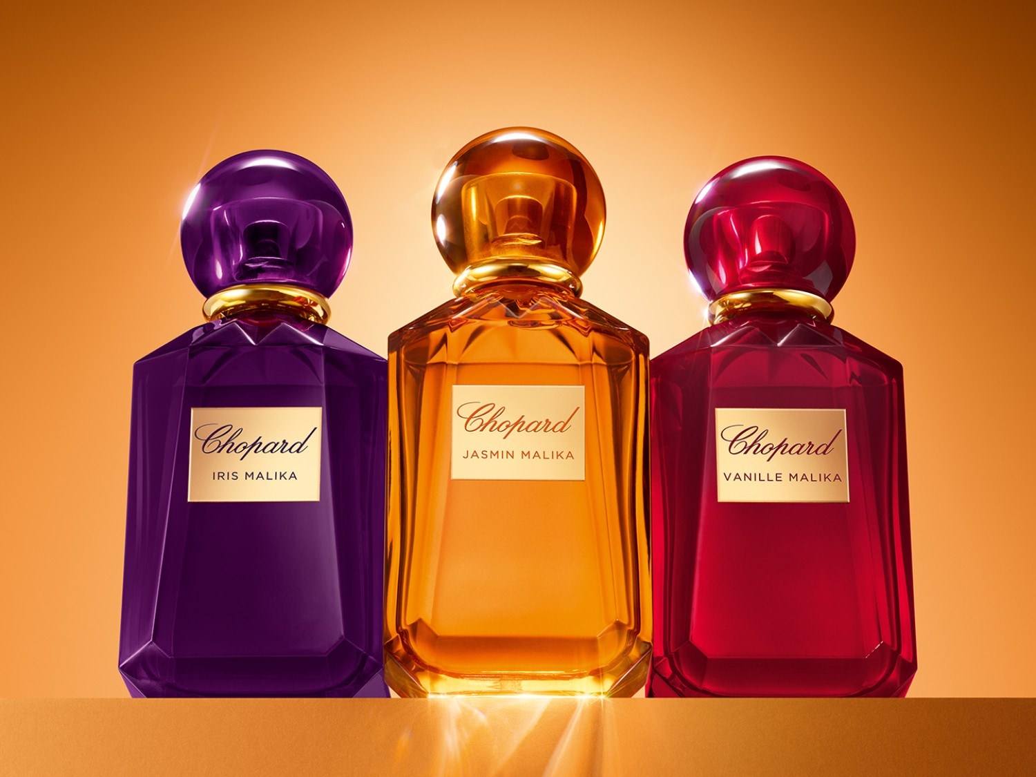 Tři flakony parfému Chopard: fialový Iris Malika, oranžový Jasmin Malika a červený Vanille Malika, každý s lesklým uzávěrem a zlatým štítkem.