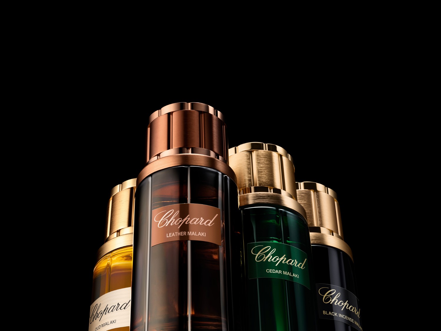 Čtyři flakony parfému Chopard Malaki v odstínech zlaté, hnědé, zelené a černé s kovovými uzávěry, které slibují luxusní zážitek.