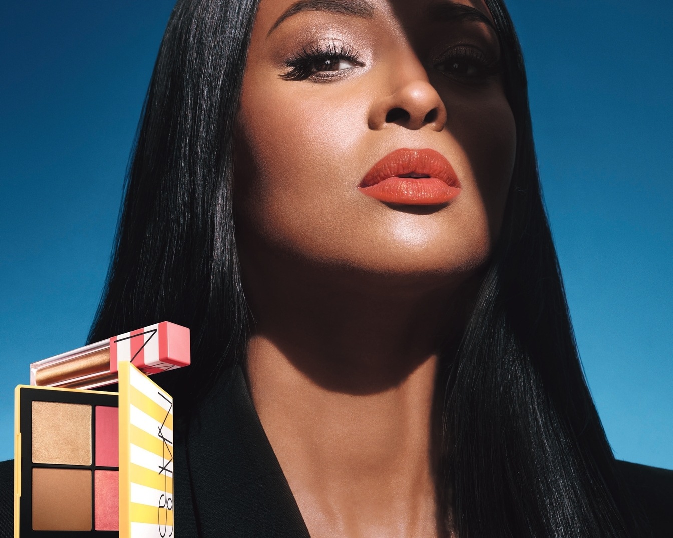 Nahaufnahme einer Frau mit glänzenden Lippen und strahlendem Teint, mit einer NARS-Palette und einem Lipgloss in Gelb- und Rosatönen.