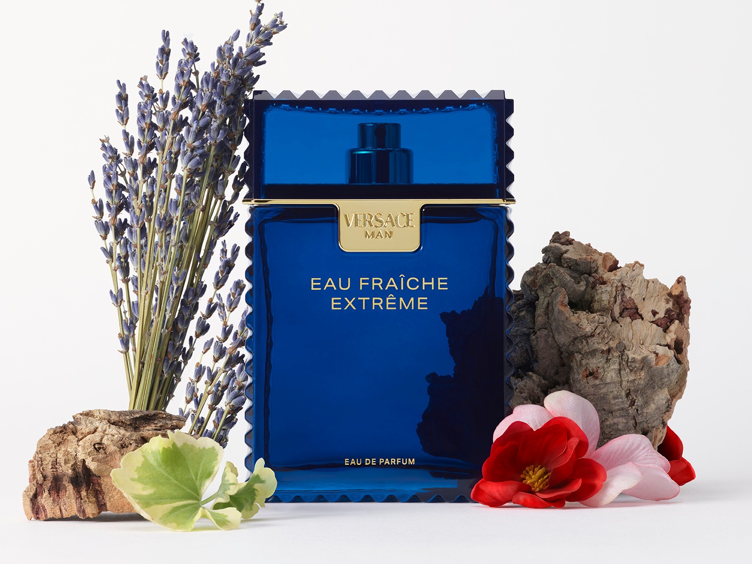 Een blauwe Versace Man Eau Fraîche Extrême Eau de Parfum fles staat tussen lavendel, bloemen en stukken boomschors.
