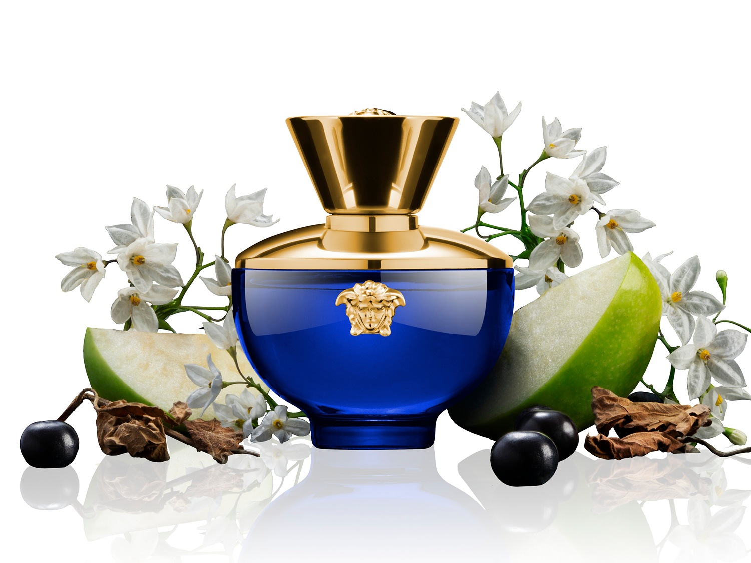 Le parfum Versace pour femme, un flacon bleu orné d'un bouchon doré, est mis en valeur avec des fleurs blanches, des tranches de pomme verte et des baies noires.