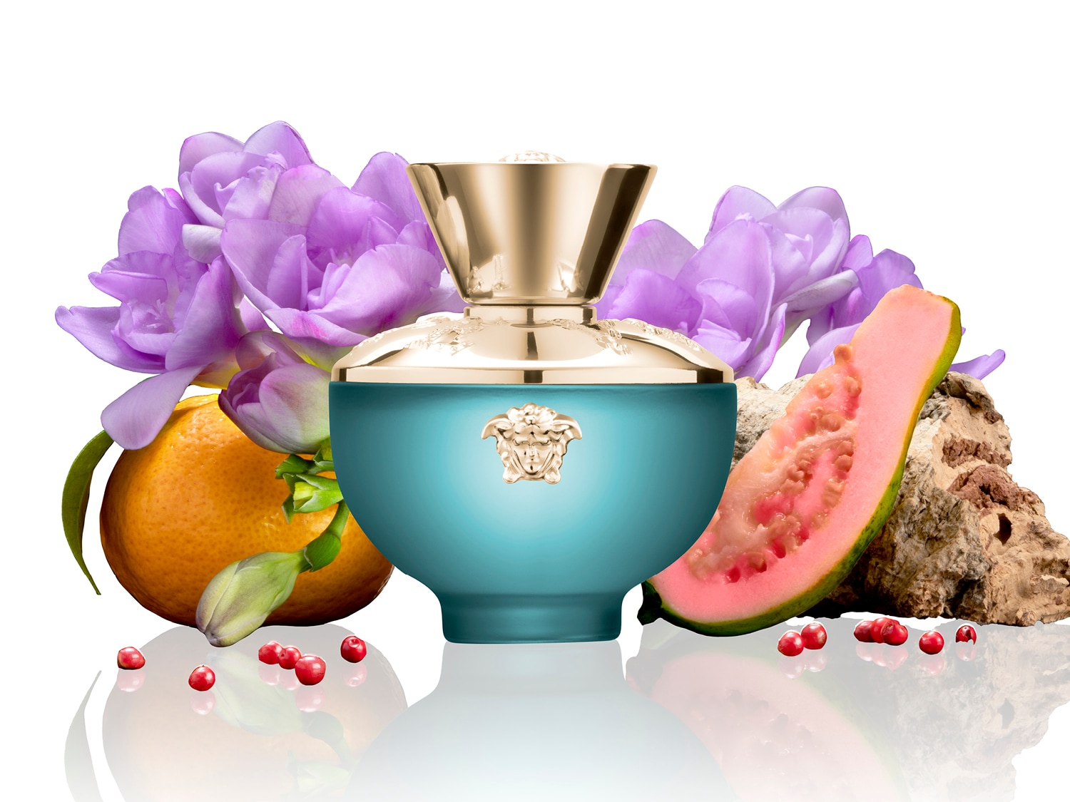 Le parfum Versace est présenté dans un flacon bleu-vert orné d'un bouchon doré, entouré de fleurs violettes, d'une orange, d'une tranche de goyave et de baies rouges.