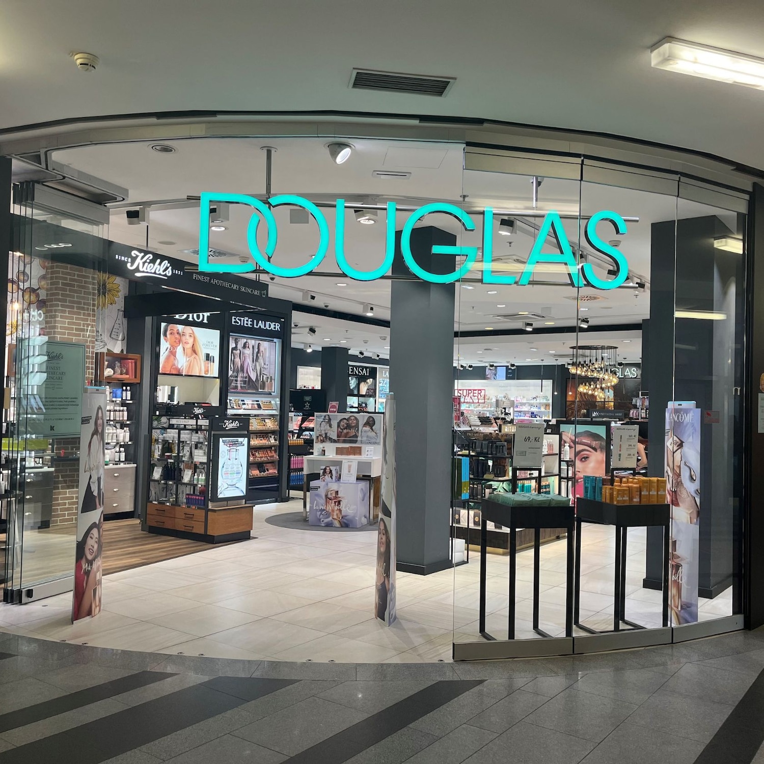 Pohled na prodejnu Douglas s modrým neonovým nápisem a širokým výběrem kosmetiky a parfémů.