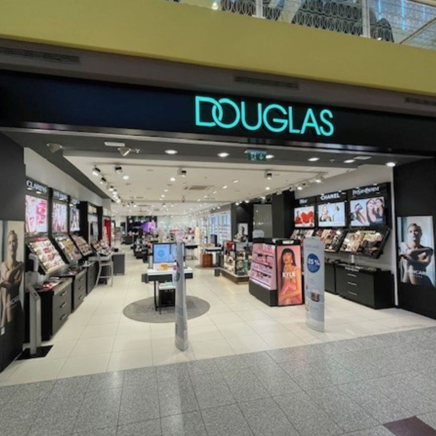 Pohled na prodejnu Douglas s osvětleným nápisem a širokým výběrem kosmetiky a vůní, které lákají k objevování krásy.