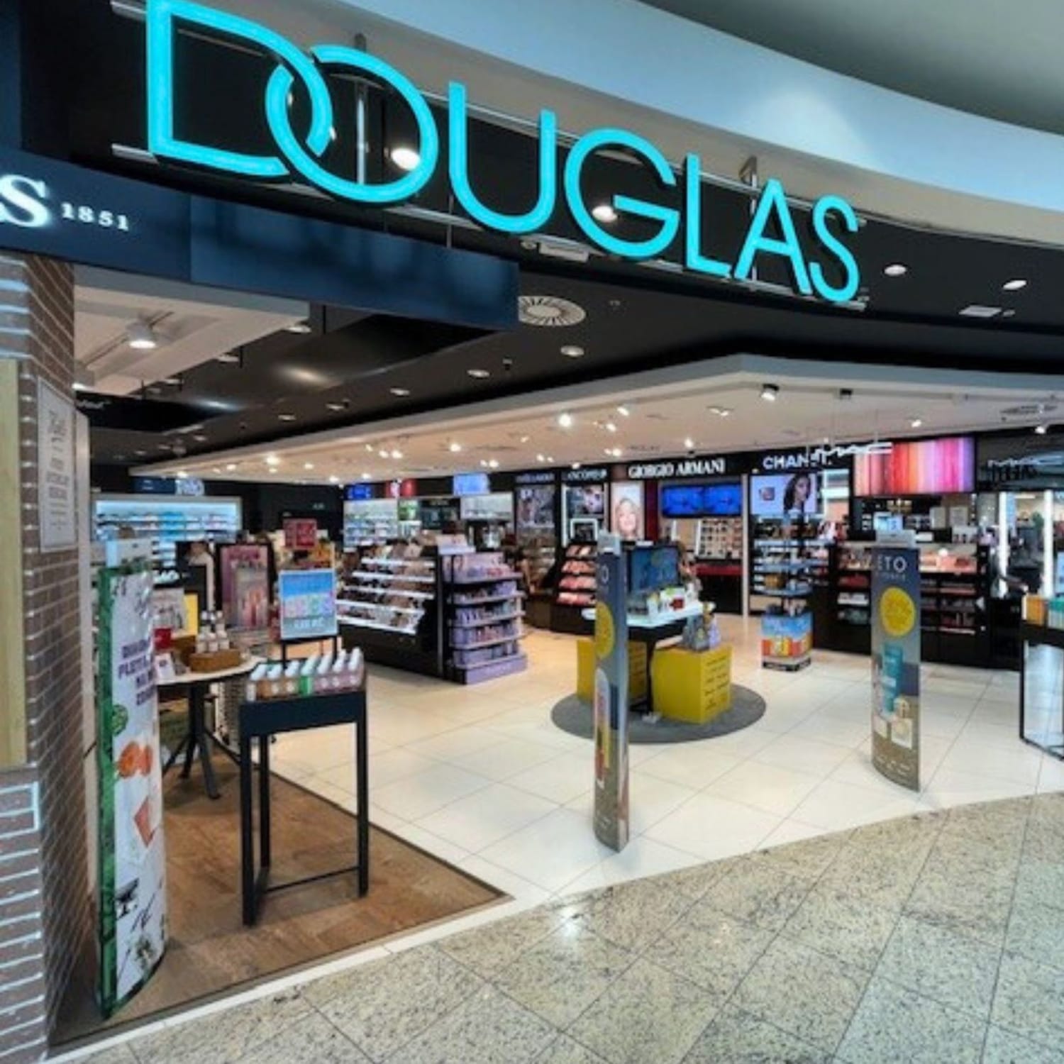 Pohled na prodejnu Douglas s modrým neonovým nápisem a širokým výběrem kosmetiky a parfémů.