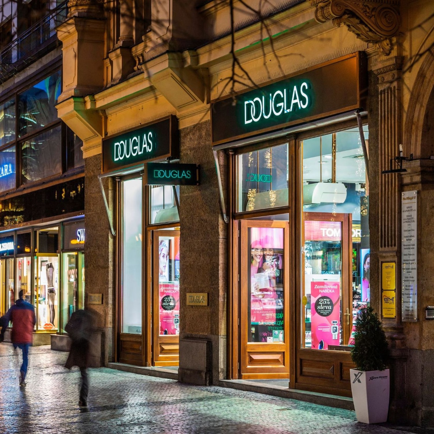 Pohled na prodejnu Douglas s osvětleným nápisem a širokým výběrem kosmetiky a vůní, které lákají k objevování krásy.